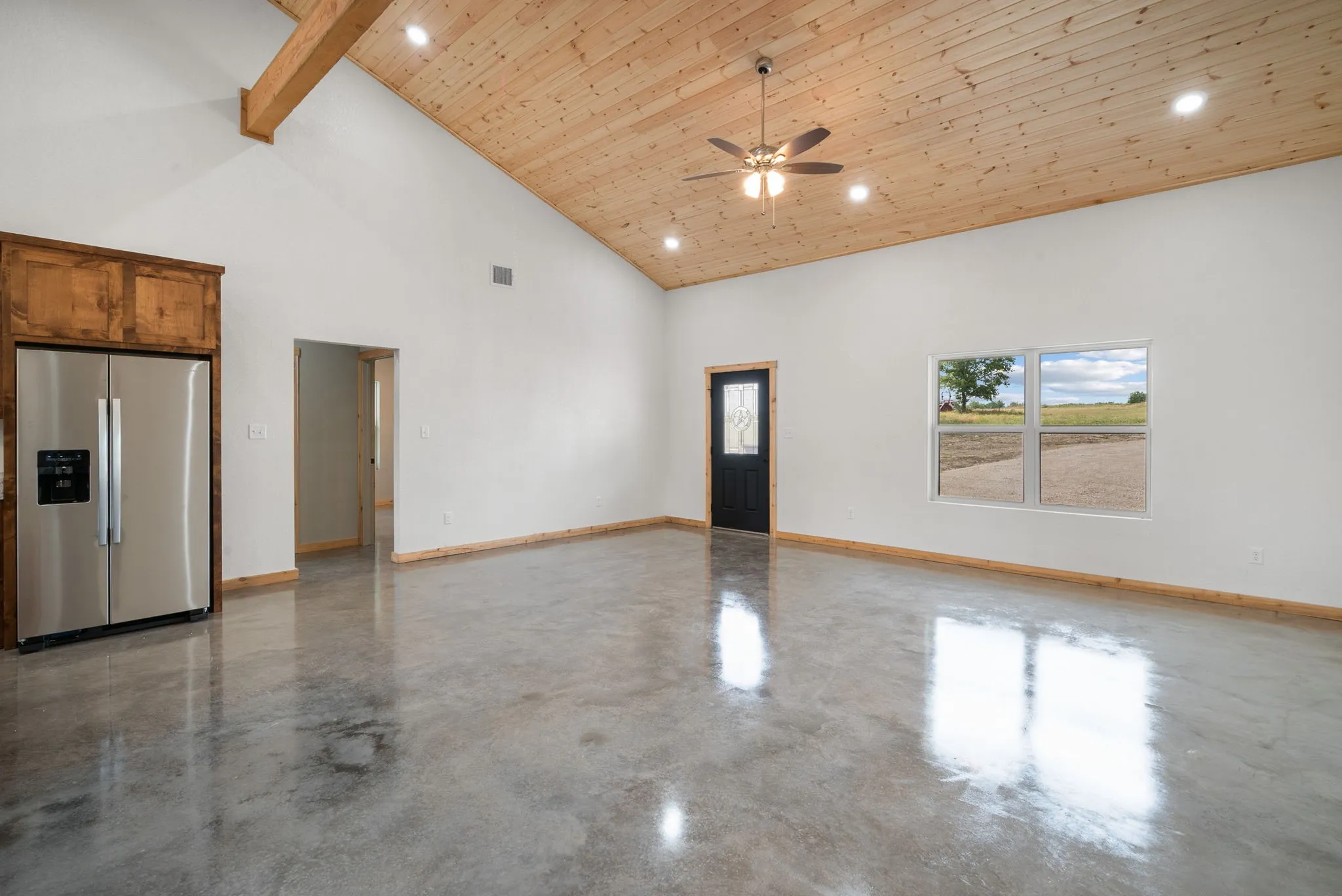 Empty room with high vaulted ceiling, beamed ceiling, concrete floors, and ceiling fan