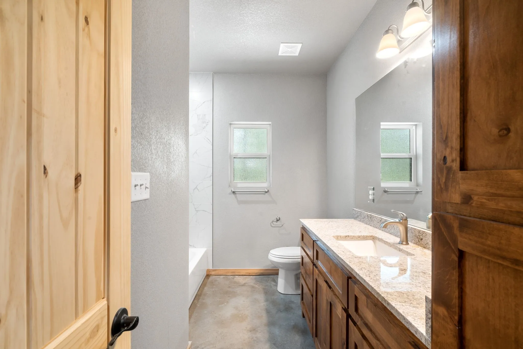 Full bathroom featuring toilet, concrete floors,  shower combination, vanity, and a textured ceiling