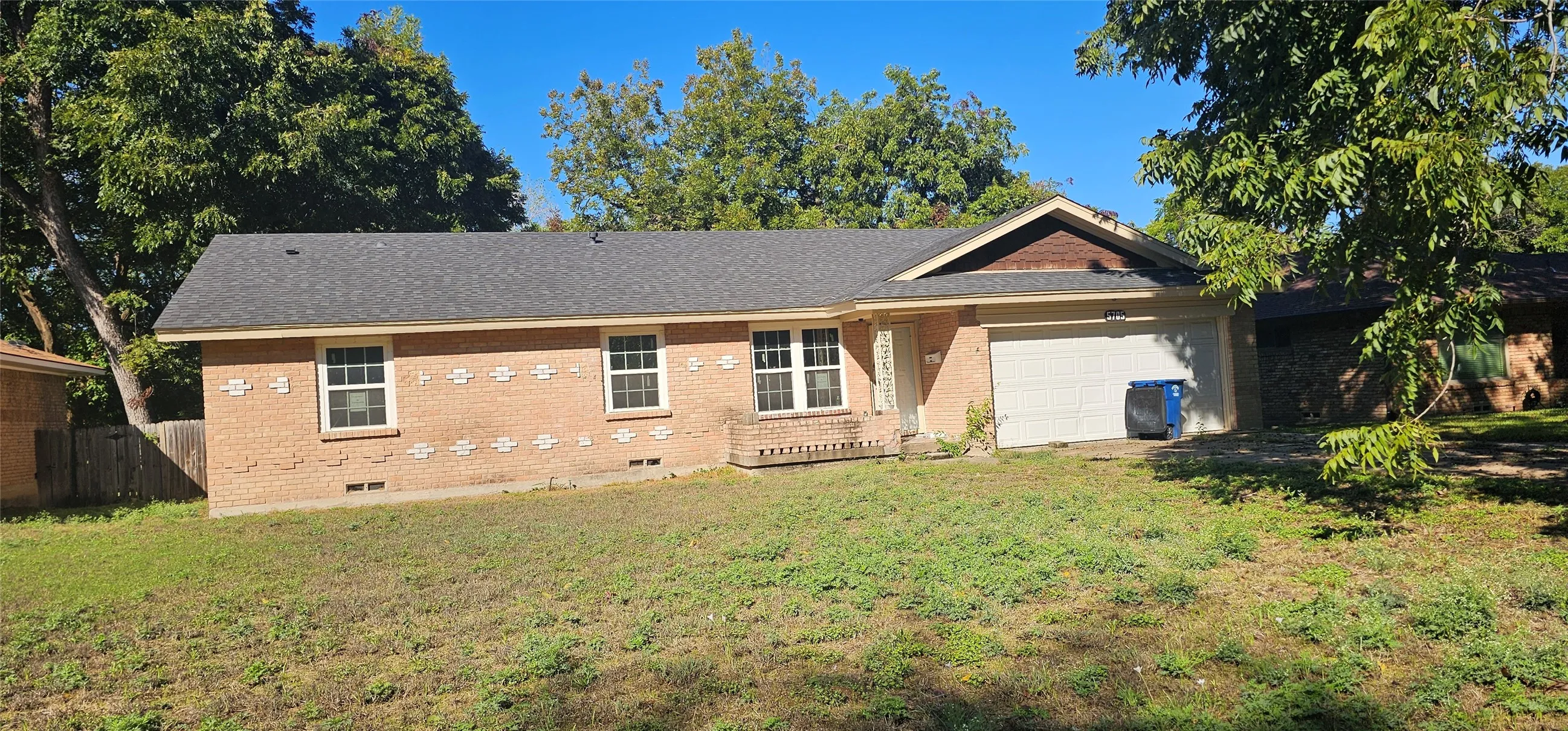 Brick exterior with decorative accents, an attached garage, and a dark shingle roof