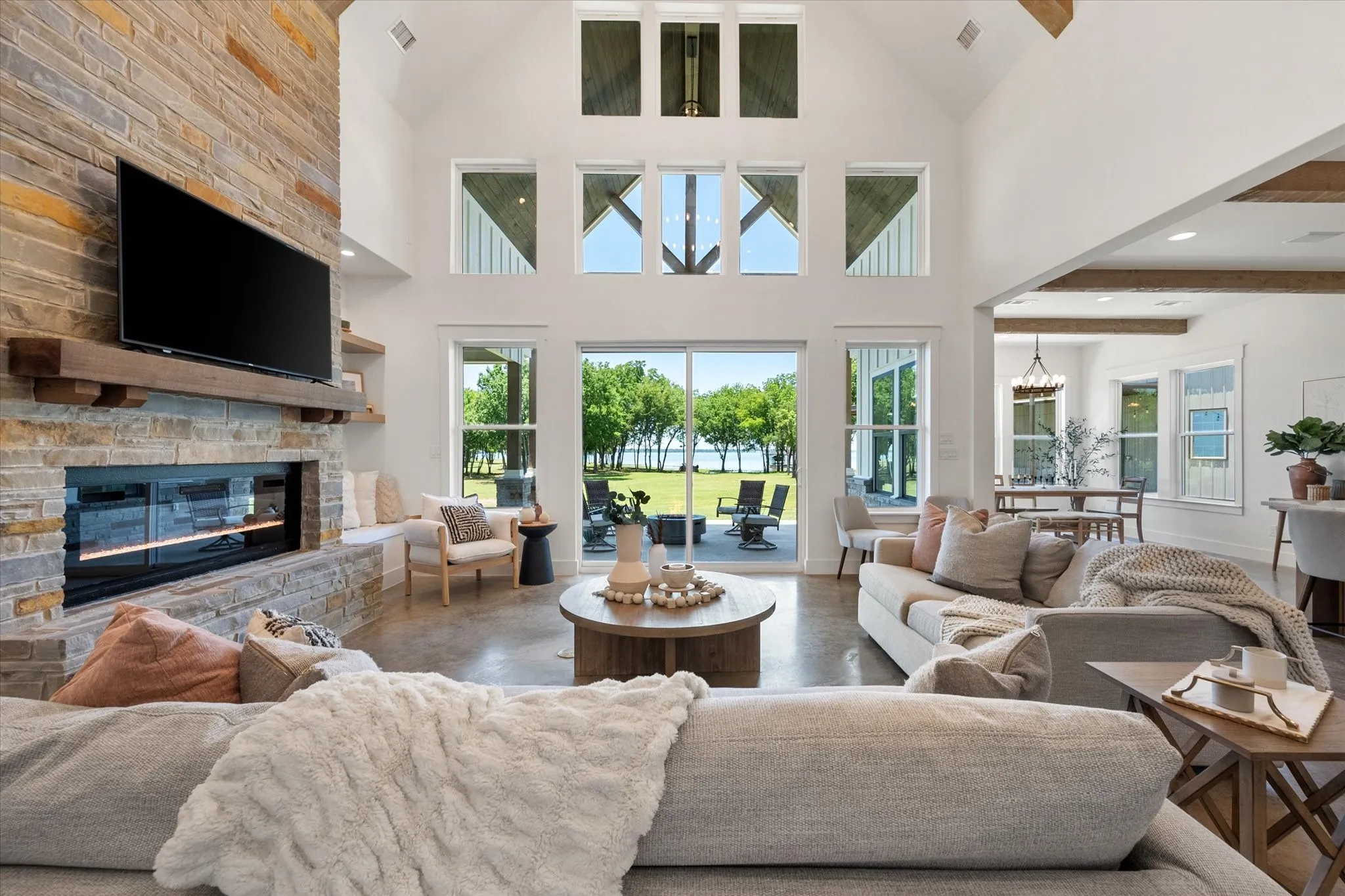 Living room with a fireplace, a notable chandelier, concrete floors, high vaulted with solid wood beams at ceiling
