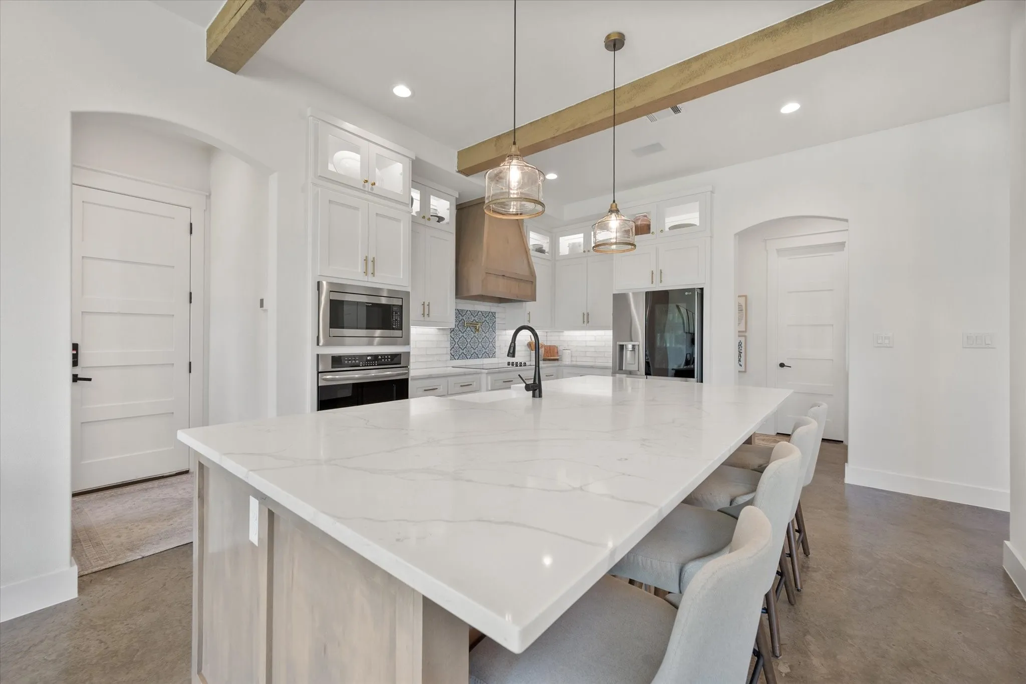 Kitchen featuring hanging light fixtures, a center island with sink, tasteful backsplash, beamed ceiling, and appliances with stainless steel finishes