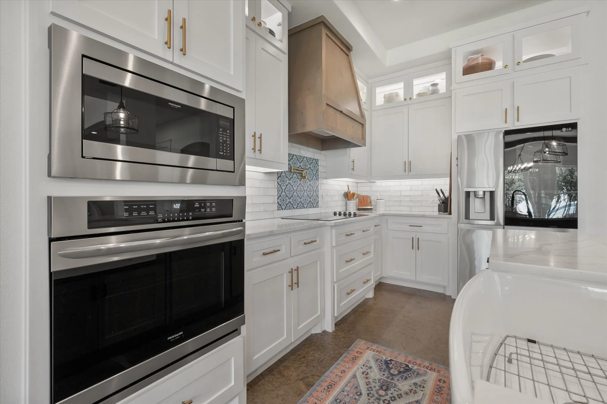 Kitchen featuring white cabinets, tasteful backsplash, custom exhaust hood, light stone countertops, and appliances with stainless steel finishes