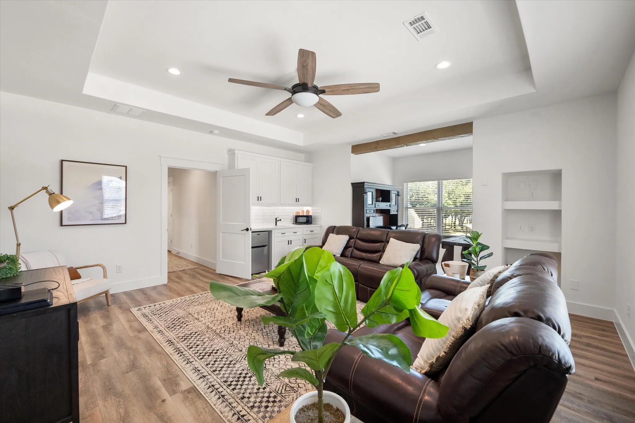 Living room with light hardwood / wood-style floors, ceiling fan, and a raised ceiling