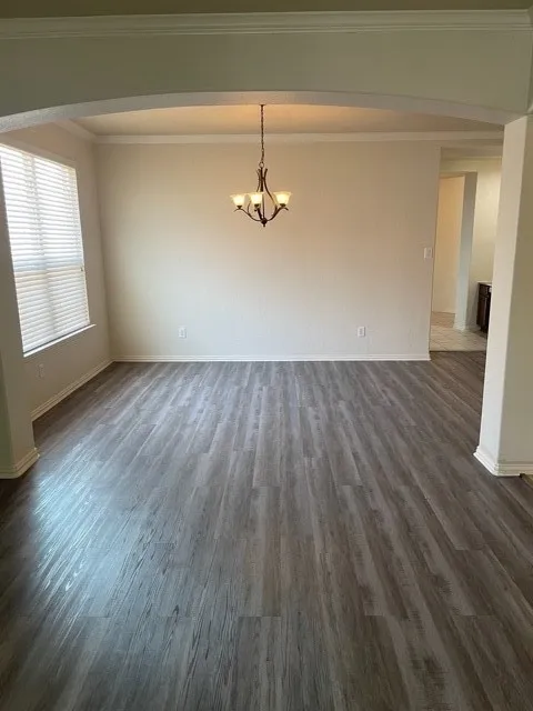 Spare room featuring dark hardwood / wood-style floors, a notable chandelier, and crown molding