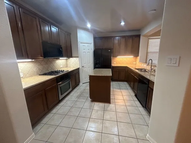 Kitchen featuring a center island, sink, backsplash, and black appliances