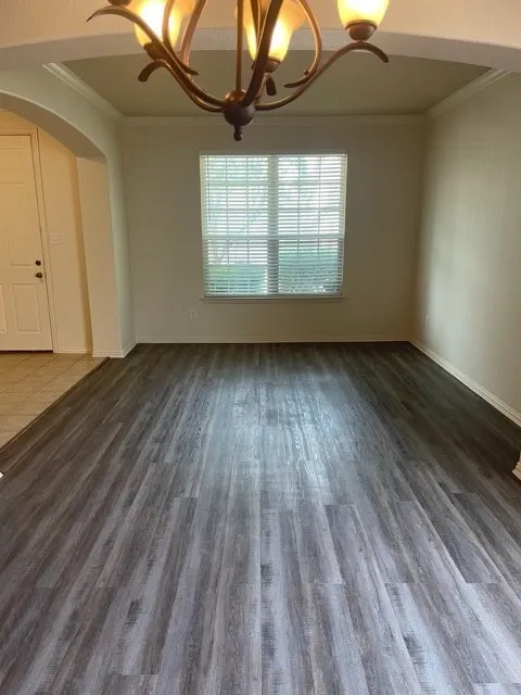 Unfurnished room featuring dark tile flooring, crown molding, and a notable chandelier