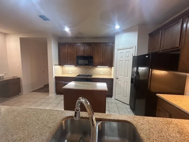 Kitchen featuring backsplash, black appliances, light tile floors, and a kitchen island