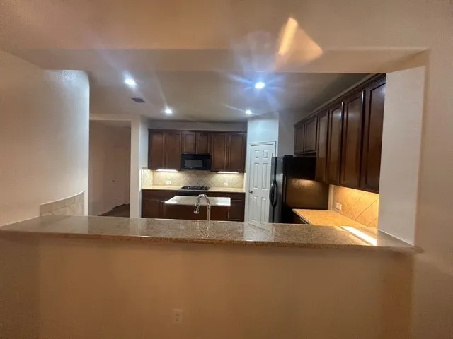 Kitchen featuring dark brown cabinetry, light stone countertops, tasteful backsplash, and black appliances