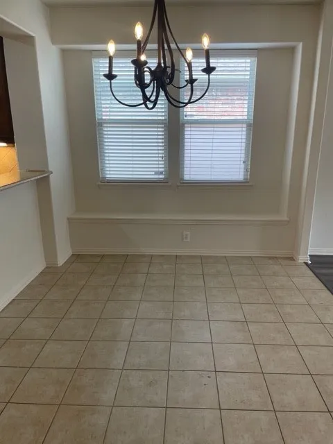 Unfurnished dining area featuring a chandelier and light tile floors
