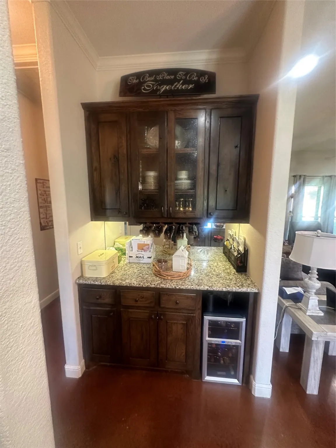 Bar with light stone counters, dark brown cabinets, beverage cooler, and crown molding