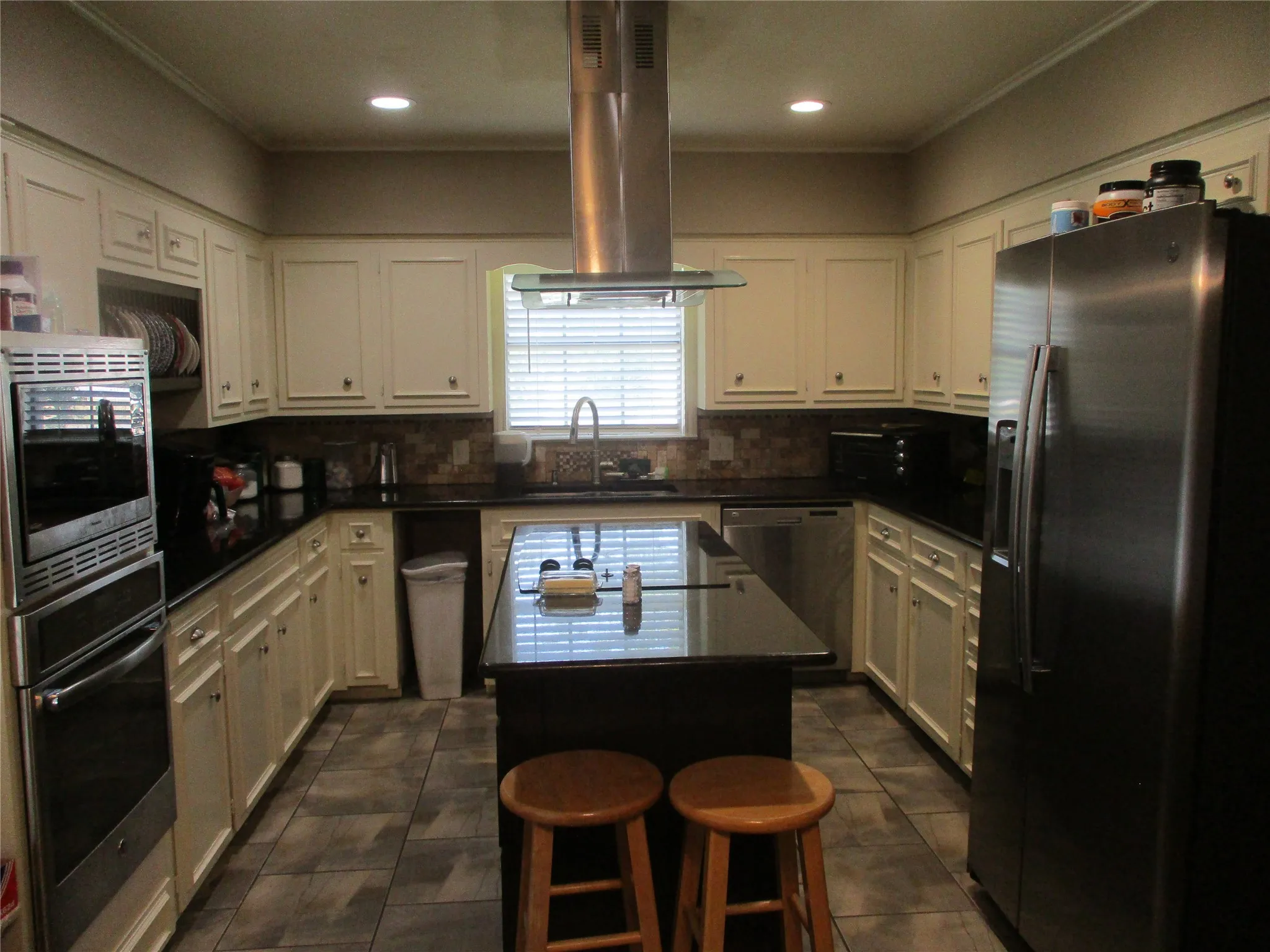 Kitchen featuring tasteful backsplash, stainless steel appliances, dark tile patterned flooring, ventilation hood, and a center island