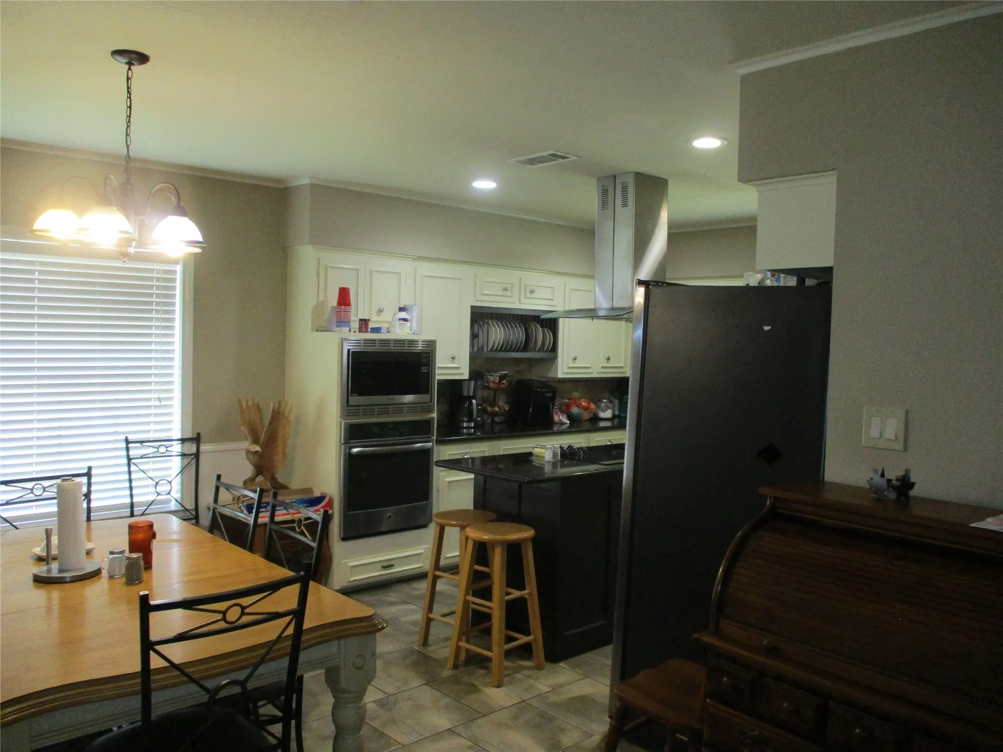 Kitchen featuring white cabinetry, wall chimney range hood, a chandelier, stainless steel appliances, and light tile patterned floors