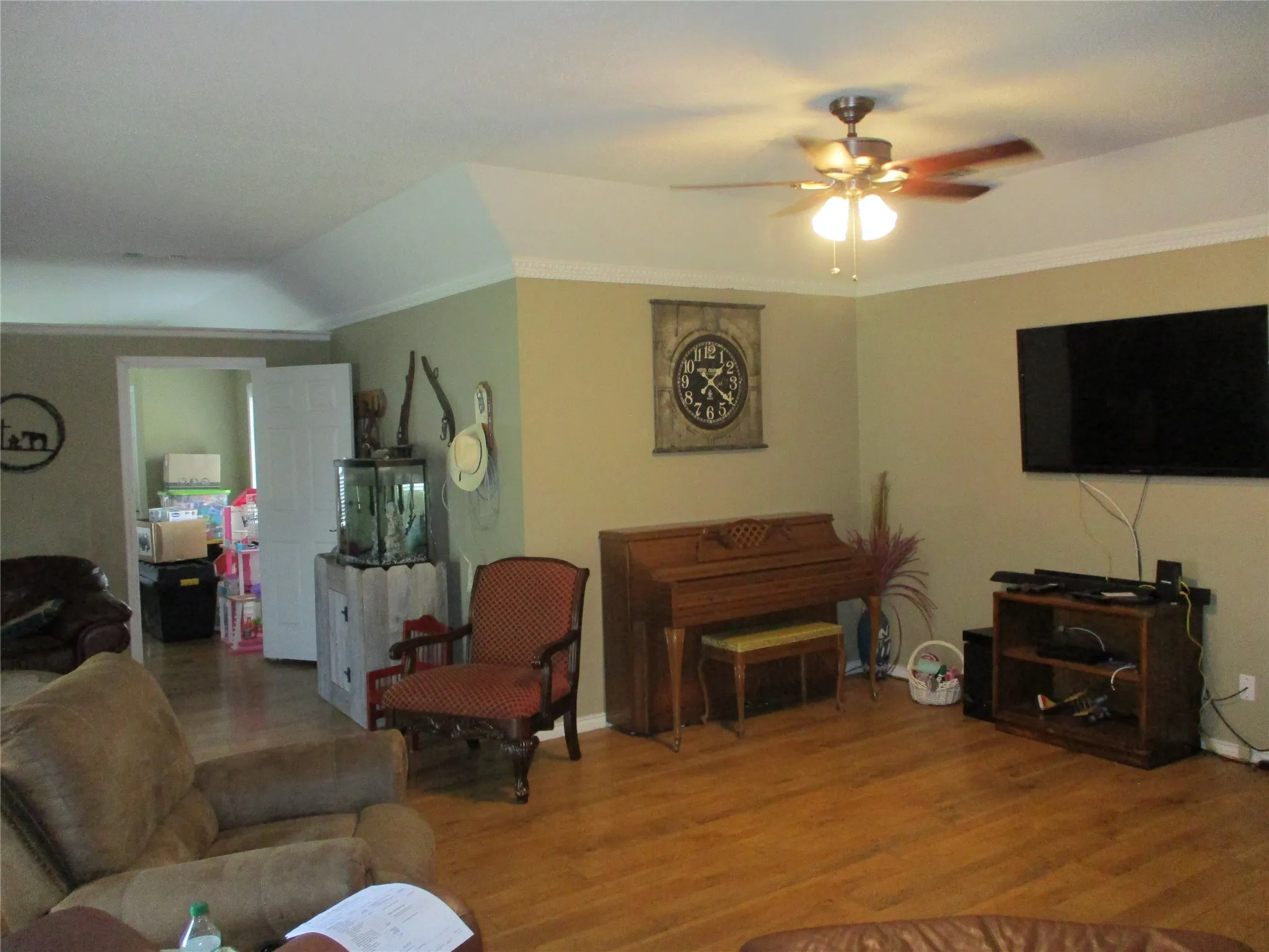 Living room with wood-type flooring, vaulted ceiling, ornamental molding, and ceiling fan