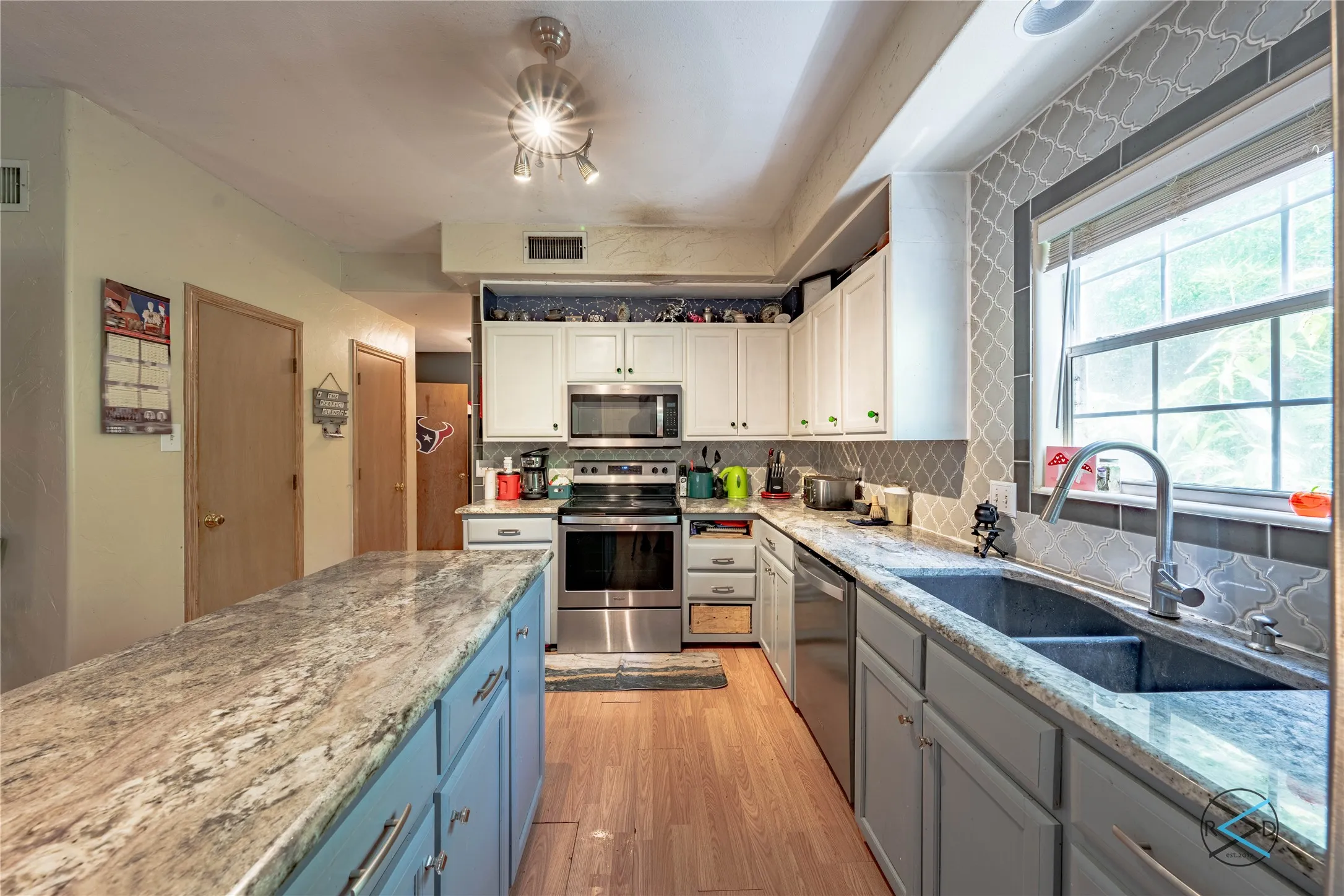 Kitchen with white cabinetry, stainless steel appliances, light hardwood / wood-style floors, decorative backsplash, and sink