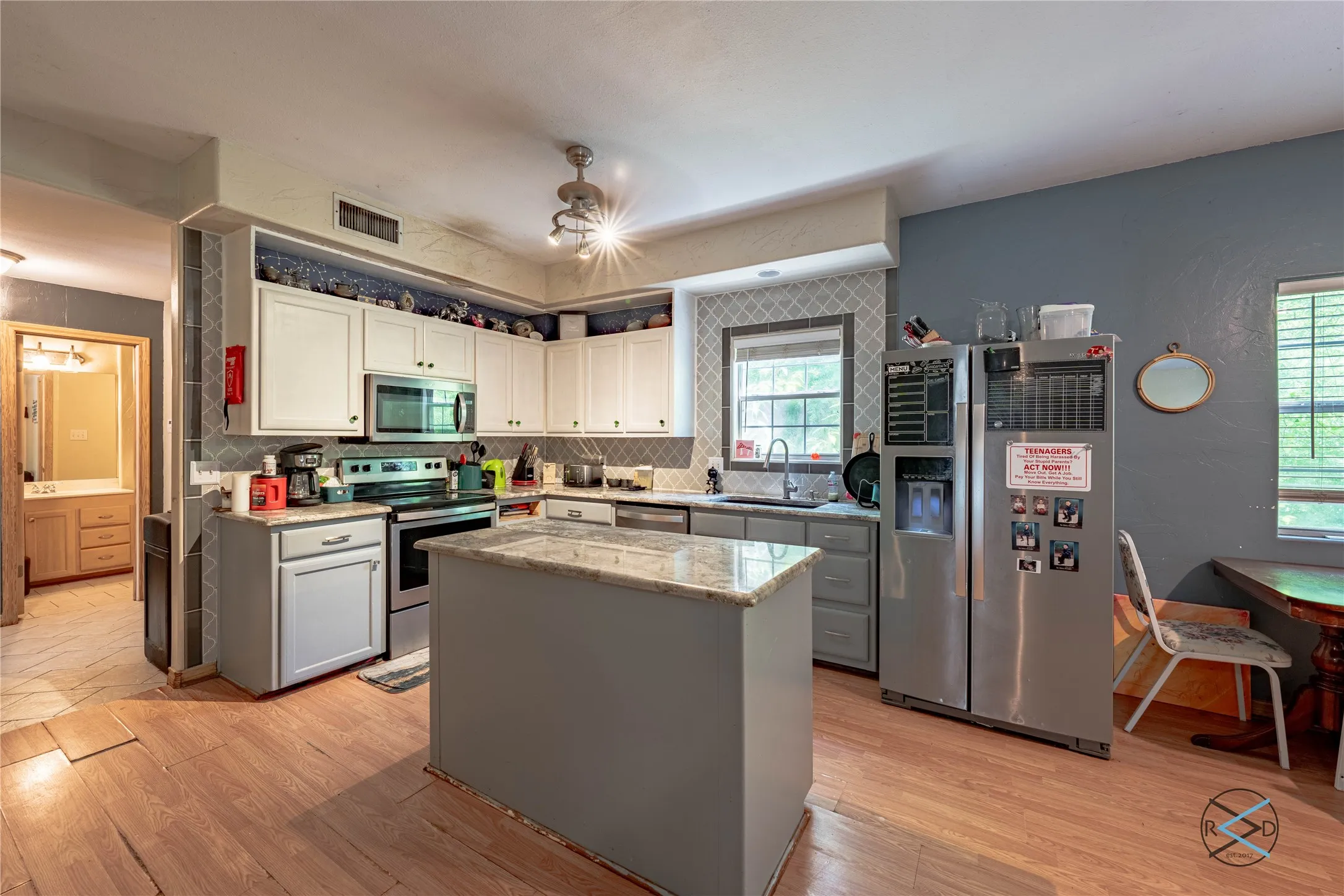 Kitchen featuring white cabinetry, tasteful backsplash, light stone counters, a kitchen island, and appliances with stainless steel finishes