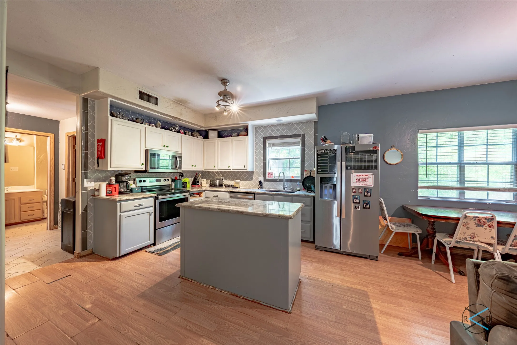 Kitchen with tasteful backsplash, stainless steel appliances, light hardwood / wood-style floors, a center island, and white cabinetry