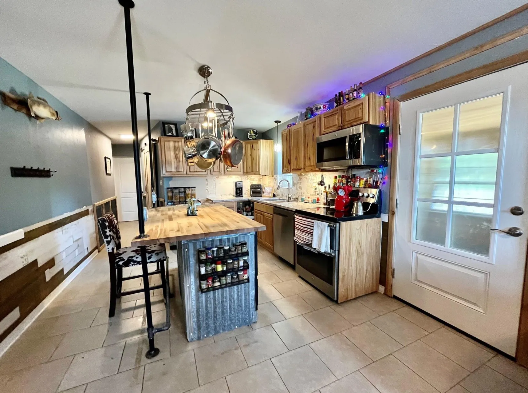 Kitchen featuring backsplash, a kitchen island, appliances with stainless steel finishes, light tile patterned floors, and wood counters