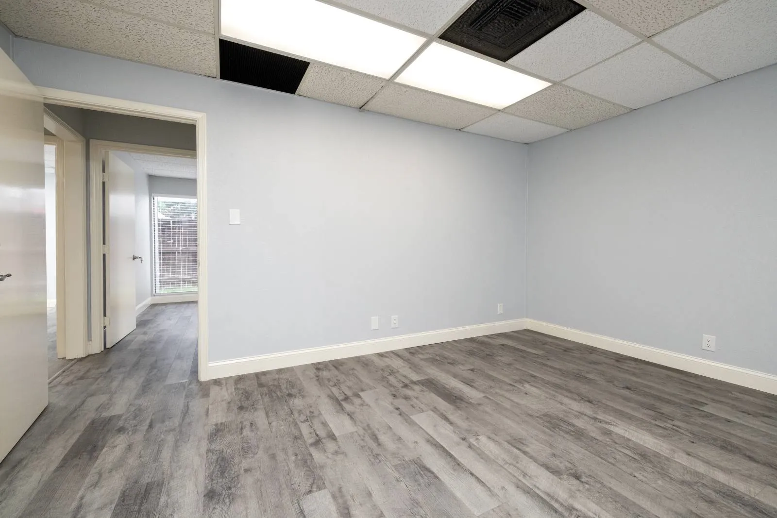 Empty room with a drop ceiling and hardwood / wood-style floors