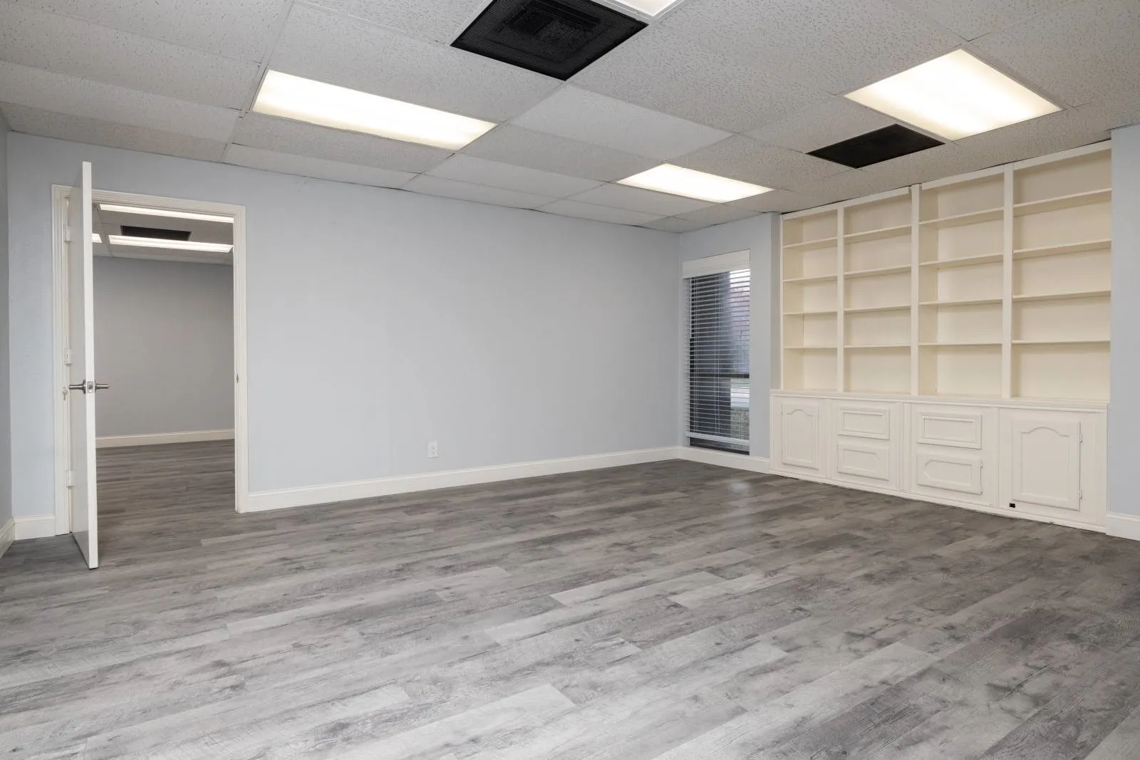 Empty room featuring wood-type flooring, a drop ceiling, and built in features