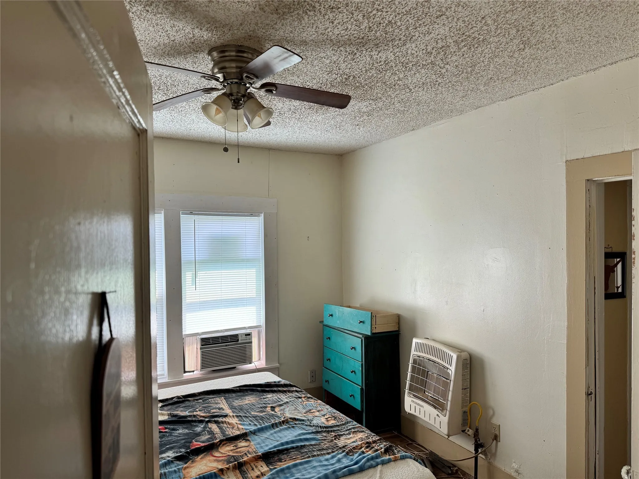 Bedroom featuring a textured ceiling, cooling unit, a wall mounted air conditioner, and ceiling fan