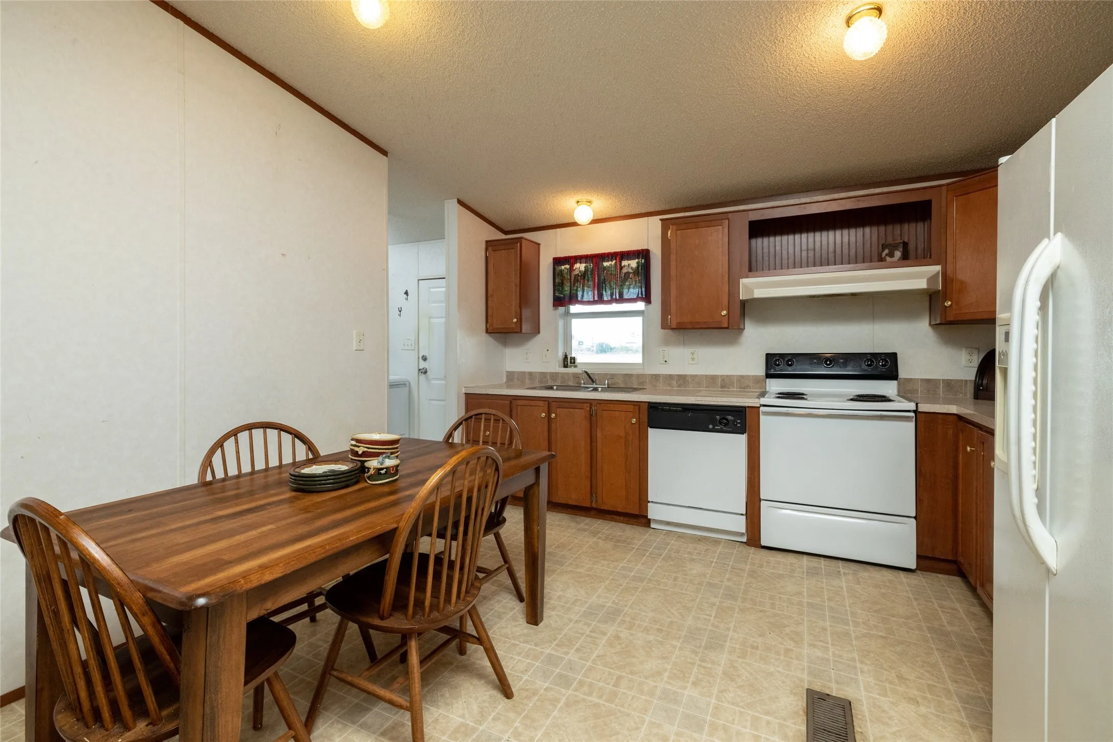Kitchen with sink, a textured ceiling, light tile patterned flooring, and white appliances