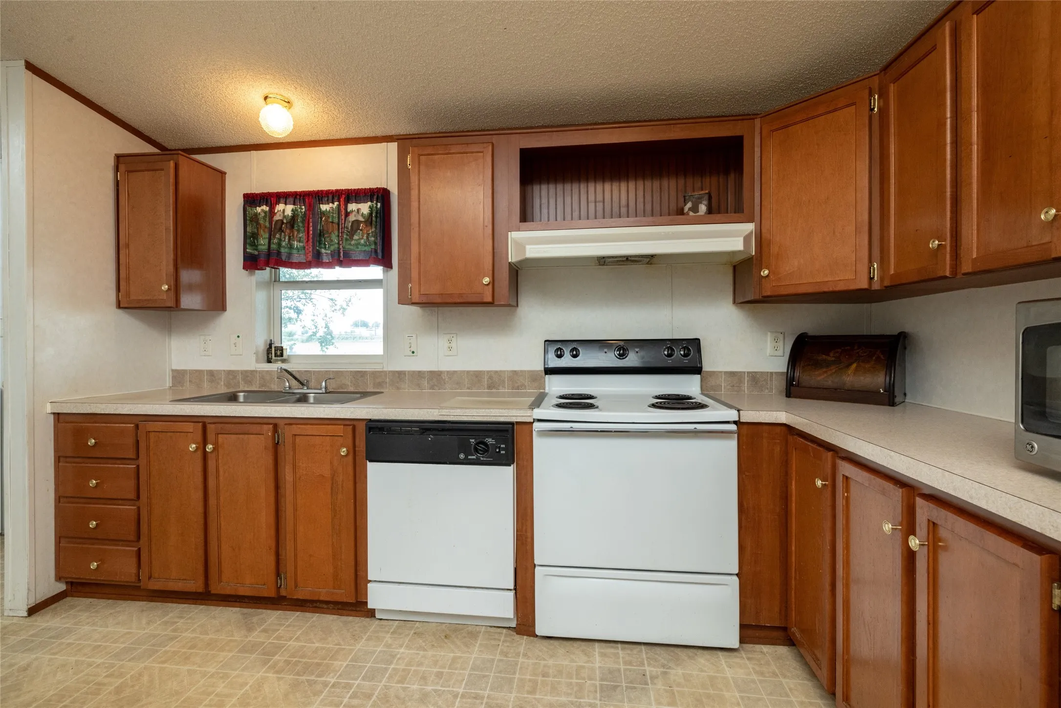Kitchen featuring a textured ceiling, white appliances, wall chimney exhaust hood, and sink