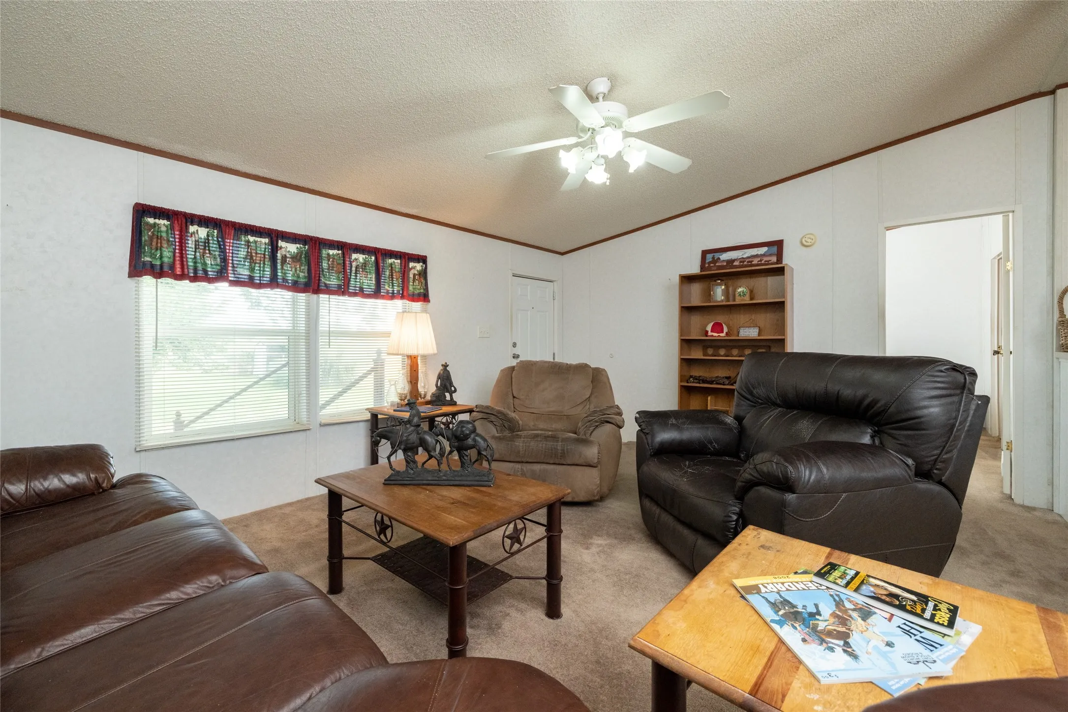 Carpeted living room featuring ceiling fan, vaulted ceiling, ornamental molding, and a textured ceiling