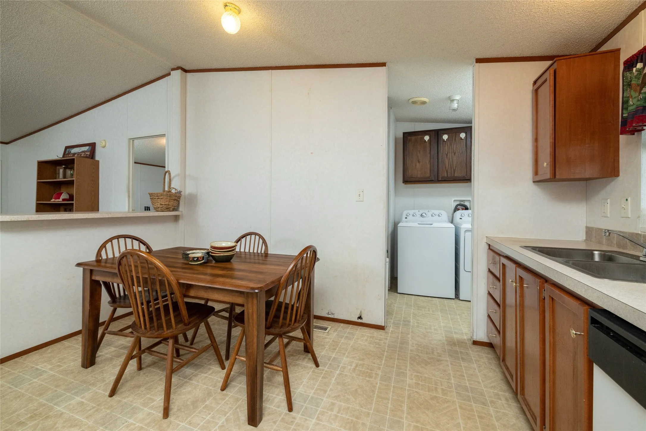 Dining area with separate washer and dryer, light tile patterned floors, sink, a textured ceiling, and lofted ceiling