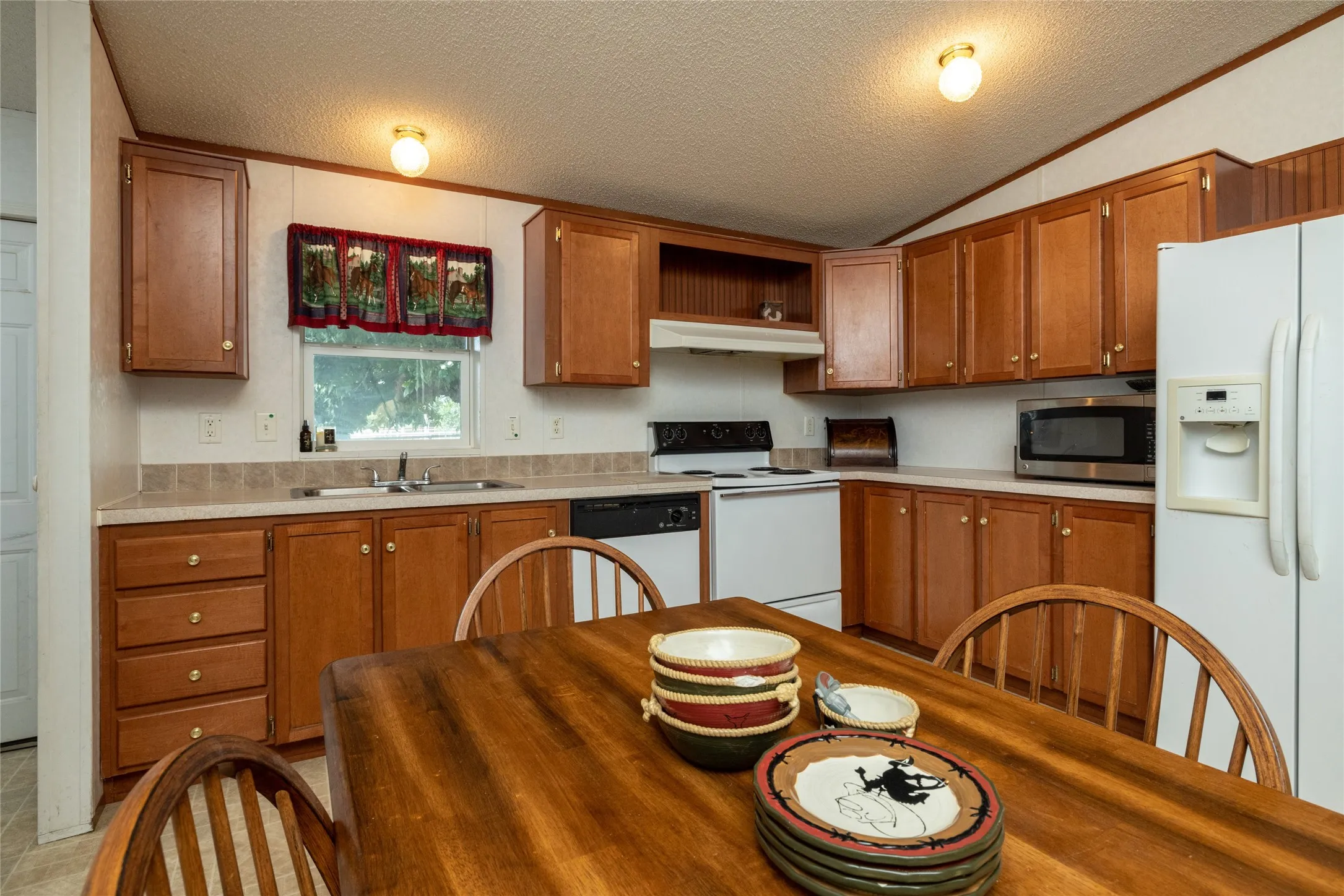 Kitchen with a textured ceiling, white appliances, vaulted ceiling, and sink