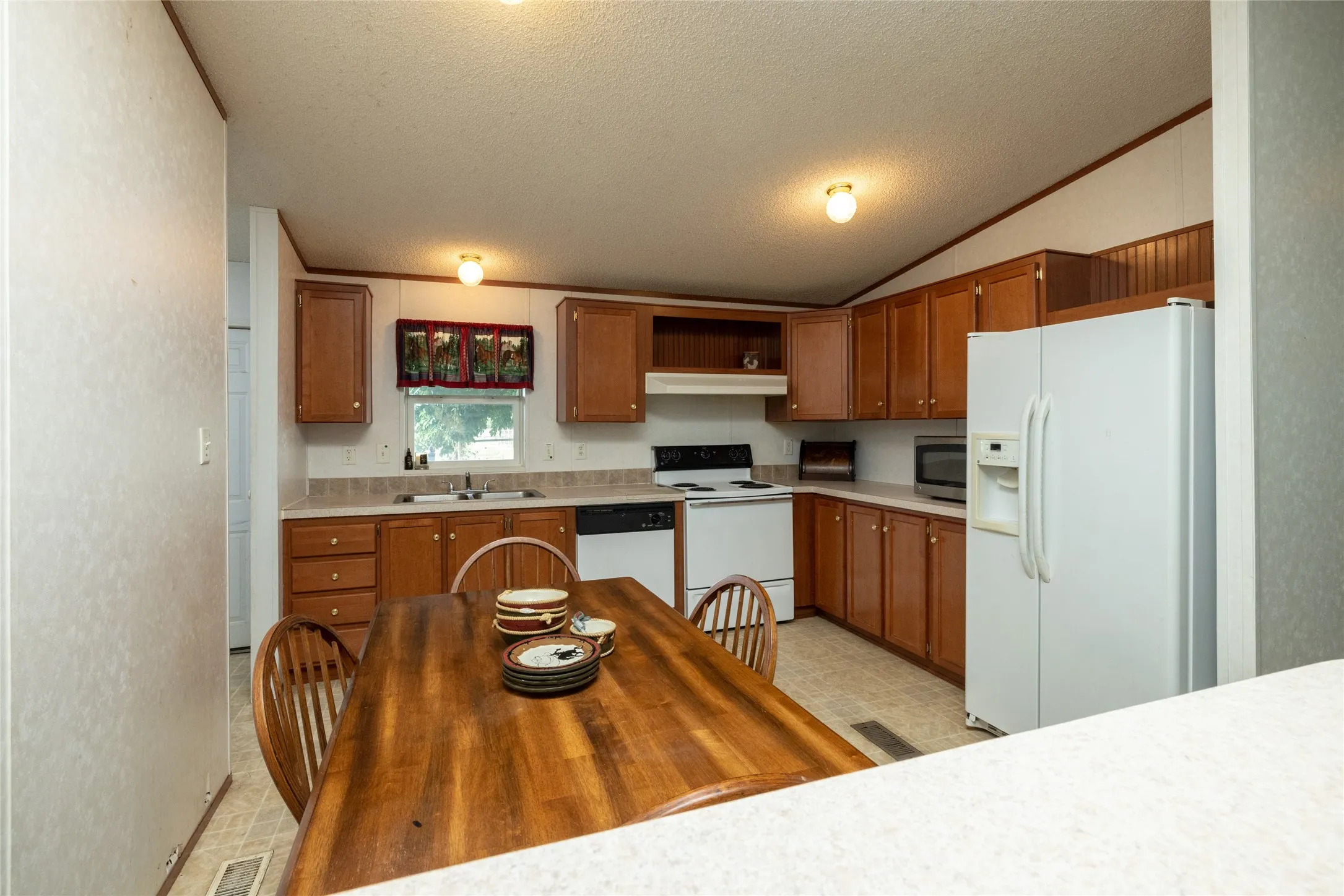 Kitchen featuring vaulted ceiling, sink, a textured ceiling, light tile patterned flooring, and white appliances