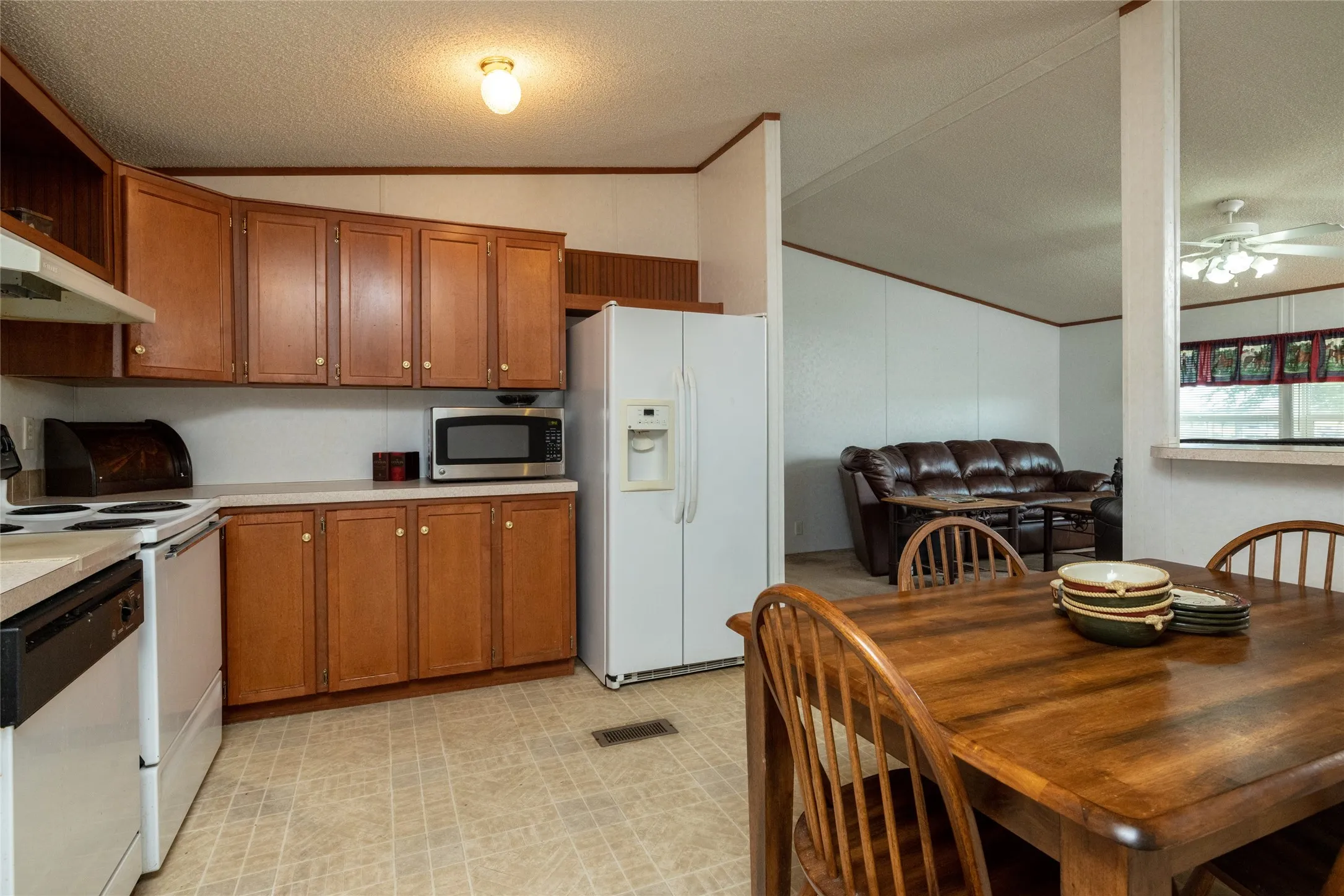 Kitchen featuring ceiling fan, vaulted ceiling, light tile patterned floors, a textured ceiling, and white appliances