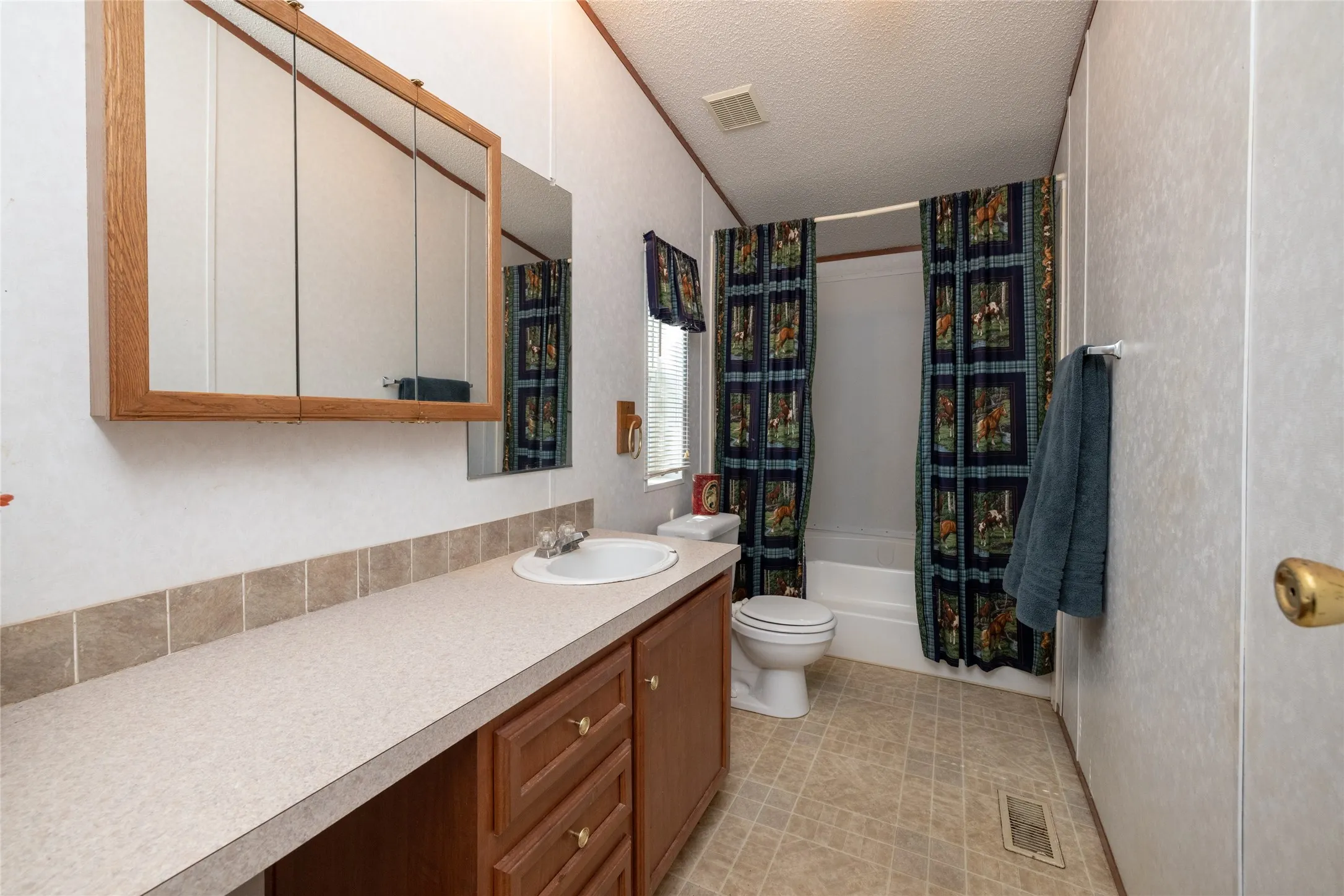 Full bathroom featuring vanity, shower / tub combo, tile patterned floors, a textured ceiling, and toilet