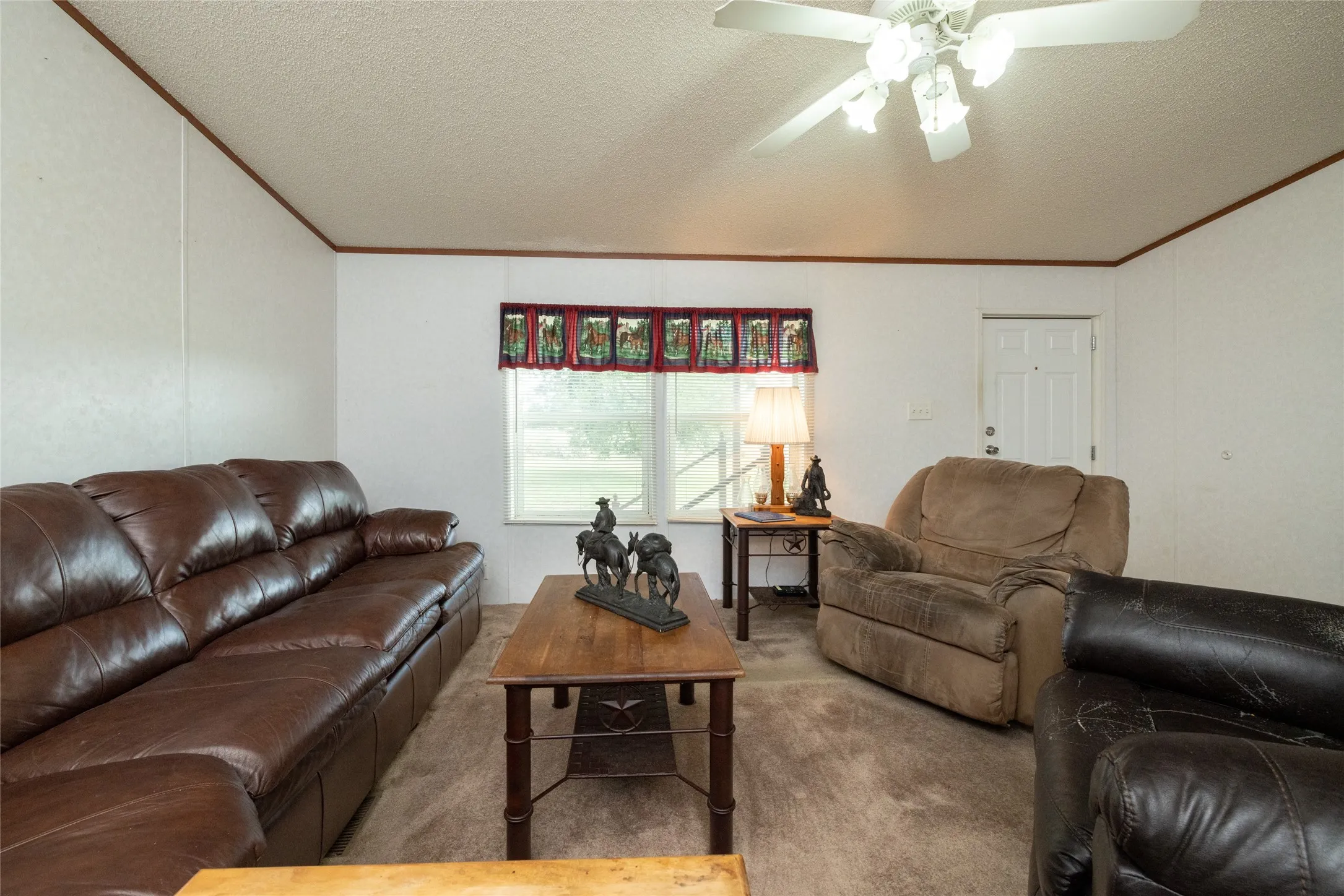 Carpeted living room with a textured ceiling, ceiling fan, and ornamental molding