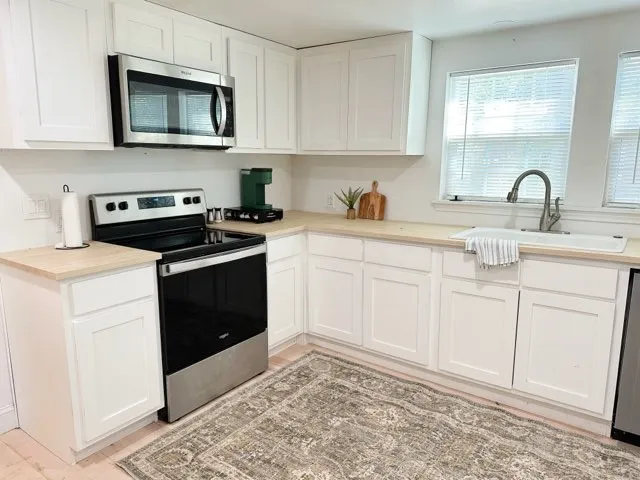 Kitchen featuring appliances with stainless steel finishes, light hardwood / wood-style floors, white cabinetry, and sink