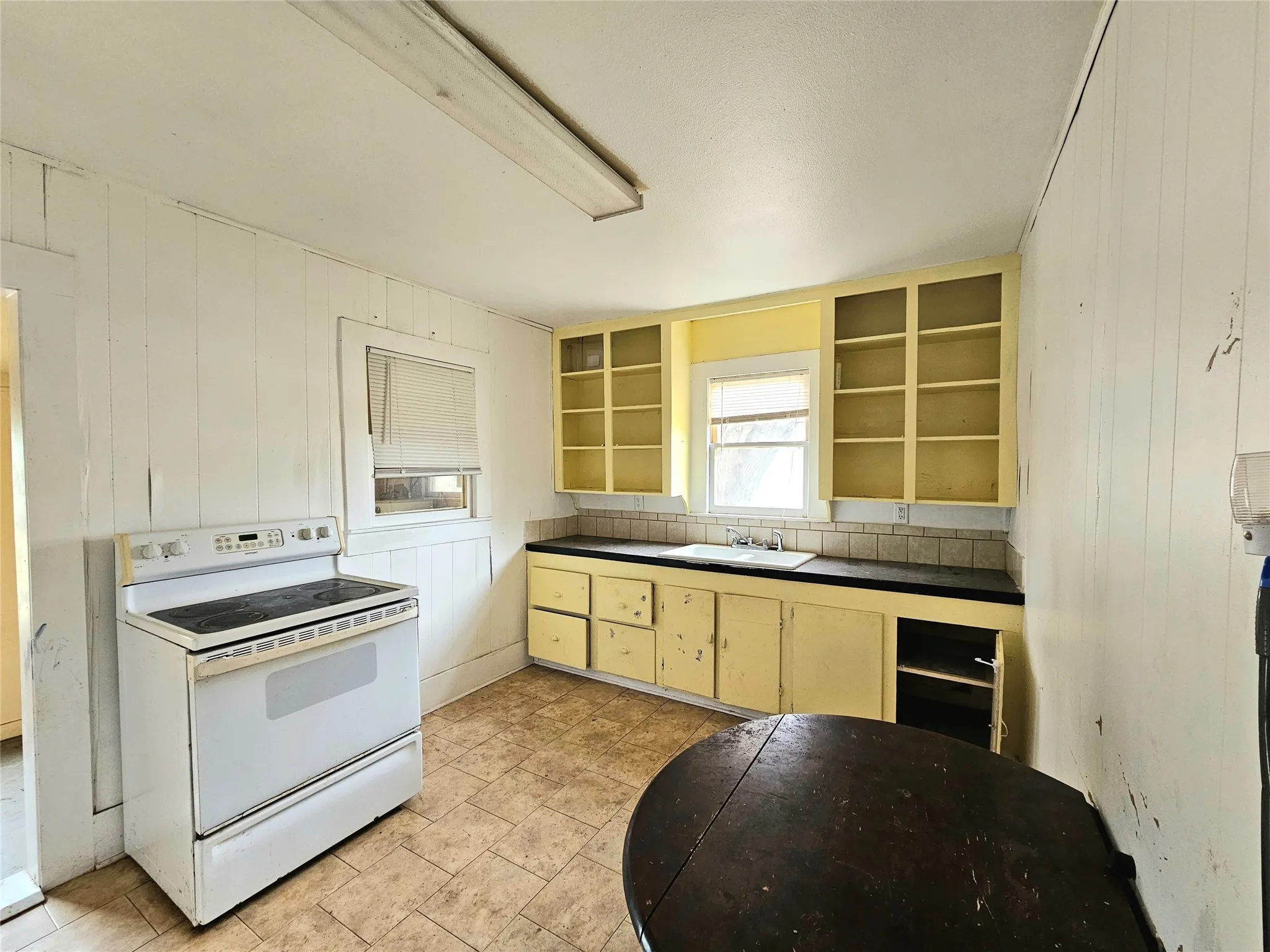 Kitchen featuring cream cabinets, open shelves, dark countertops, white electric range, and a sink