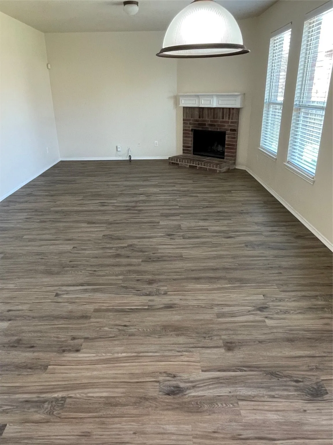 Unfurnished living room featuring dark hardwood / wood-style flooring and a brick fireplace