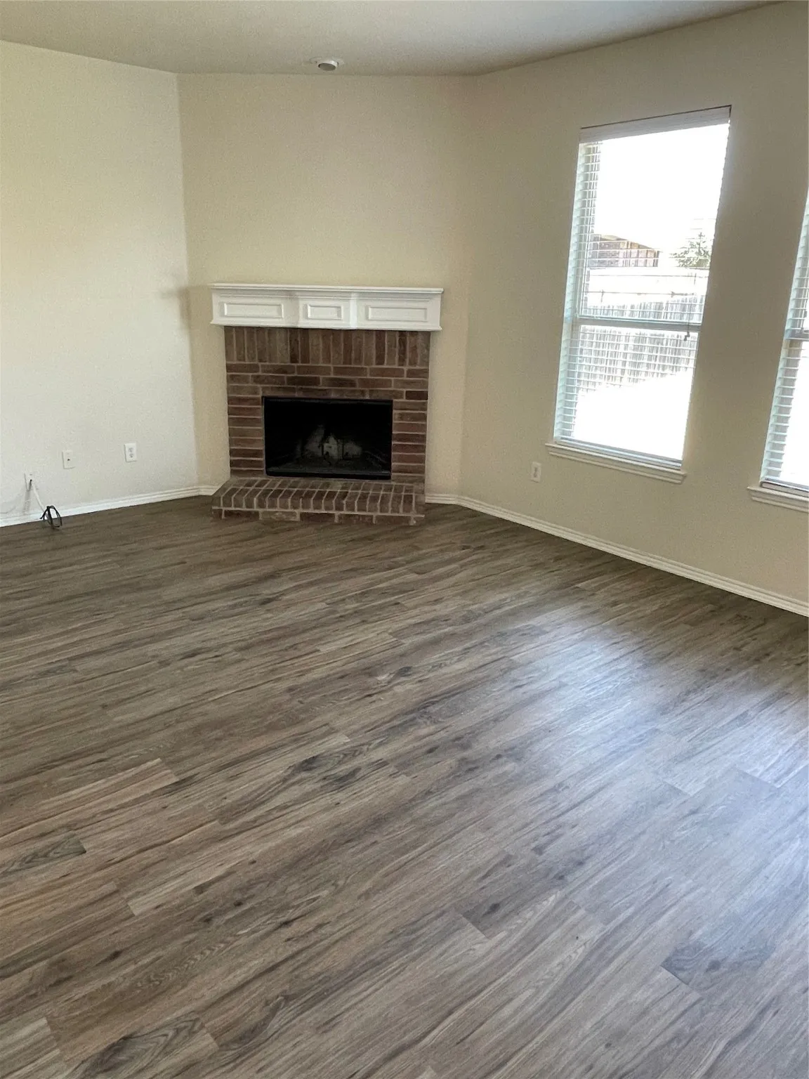 Unfurnished living room featuring dark hardwood / wood-style flooring, a brick fireplace, and a wealth of natural light