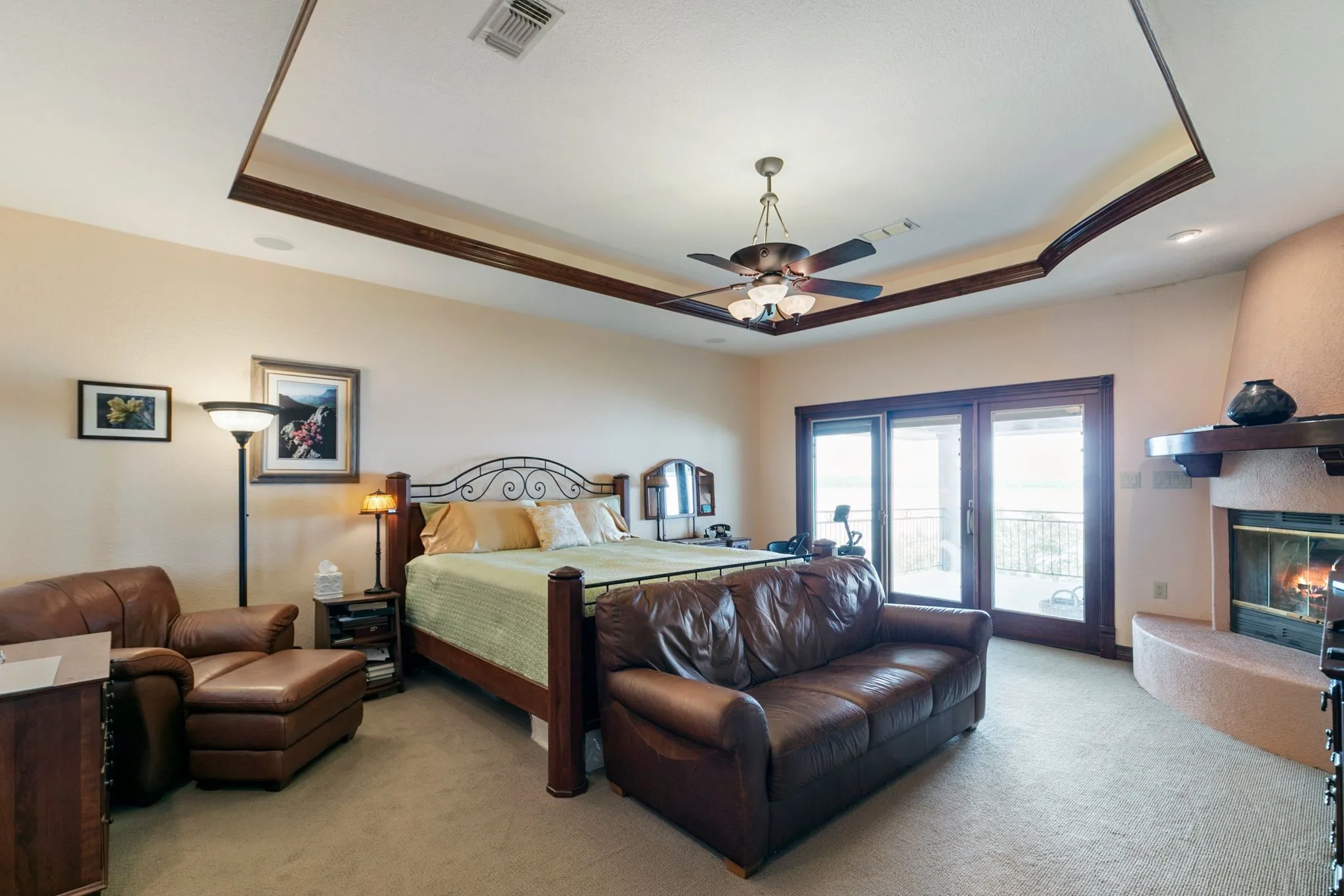 Carpeted bedroom featuring ceiling fan, a fireplace, a raised ceiling, and access to outside