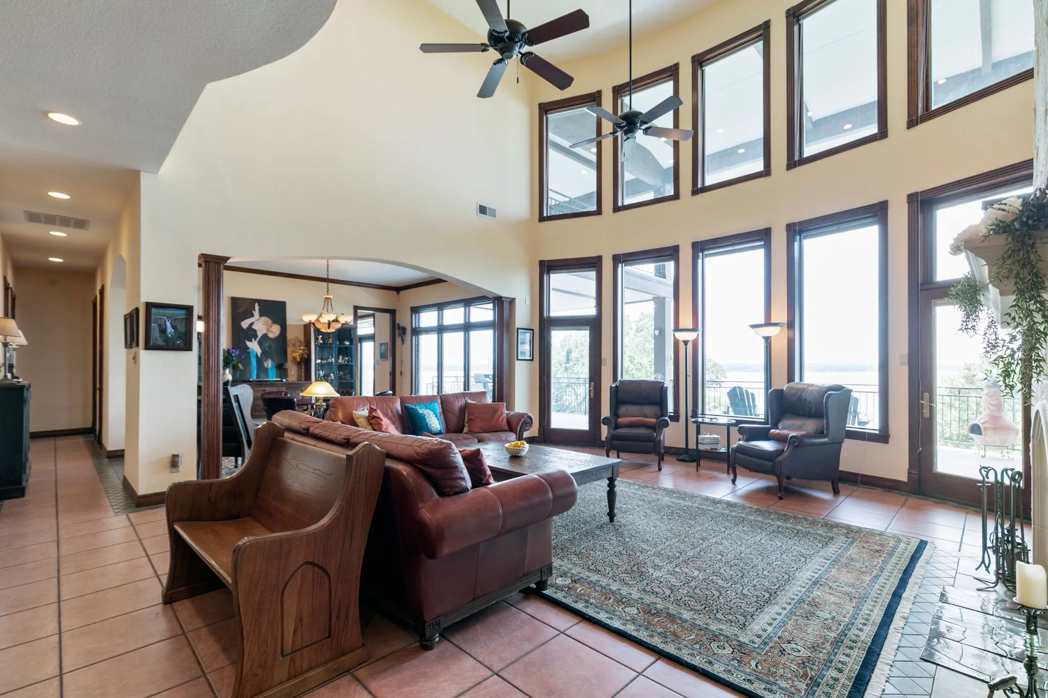 Living room featuring tile patterned flooring, a healthy amount of sunlight, a towering ceiling, and ceiling fan with notable chandelier