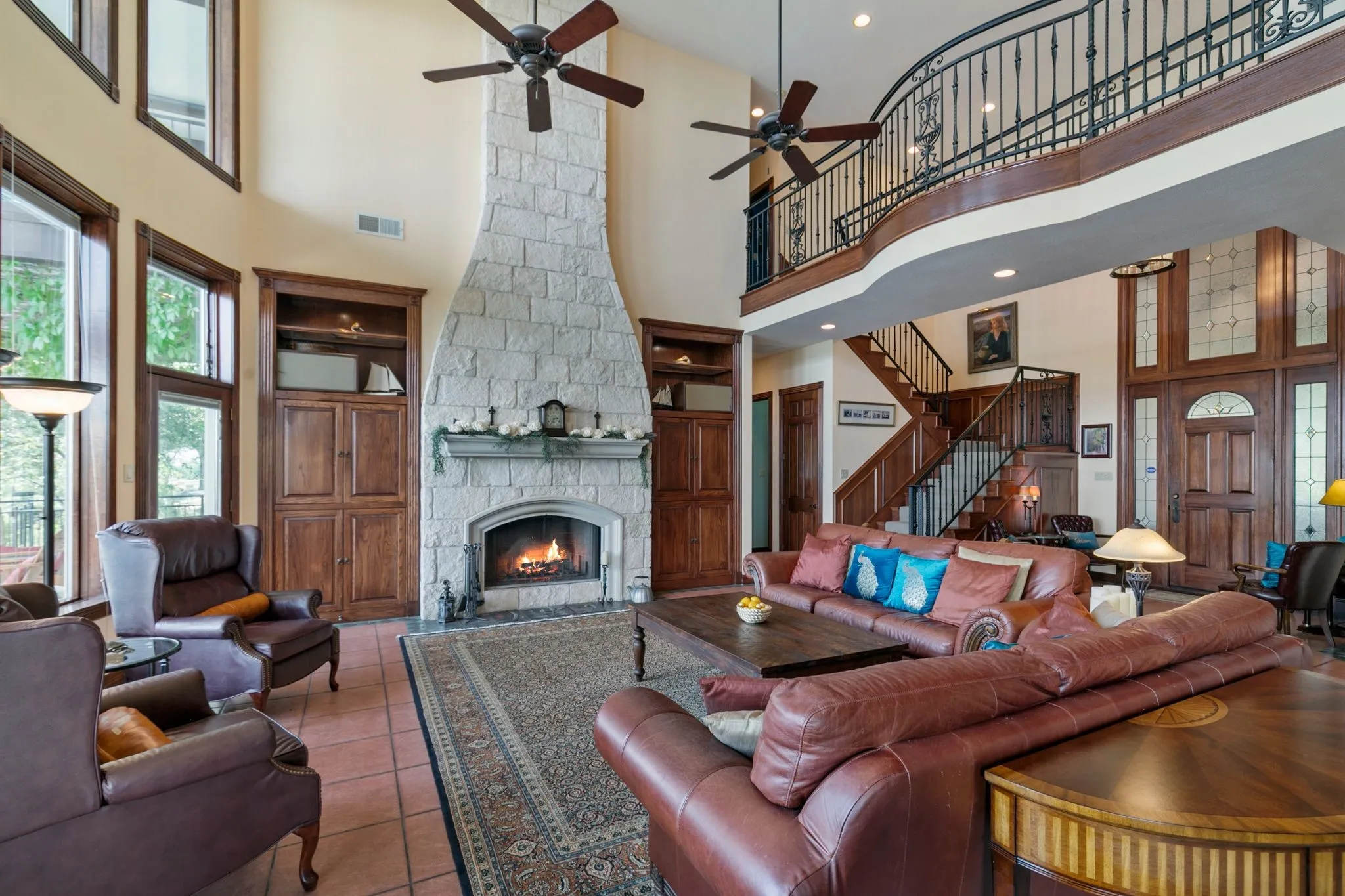 Tiled living room with ceiling fan, a towering ceiling, and a stone fireplace