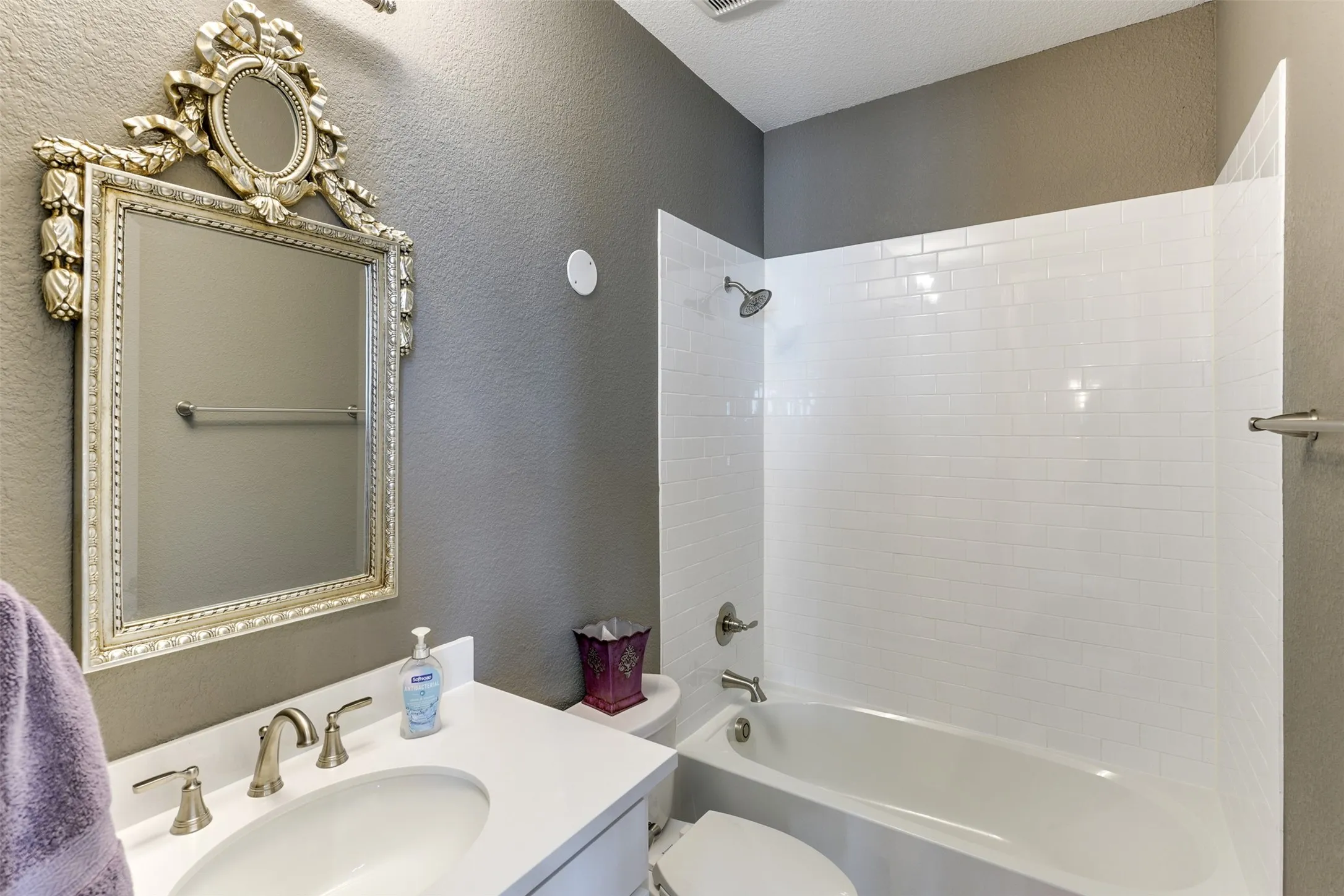 Full bathroom featuring vanity, tiled shower / bath, a textured ceiling, and toilet.  Services the downstairs bedroom and the family, kitchen, and dining areas.