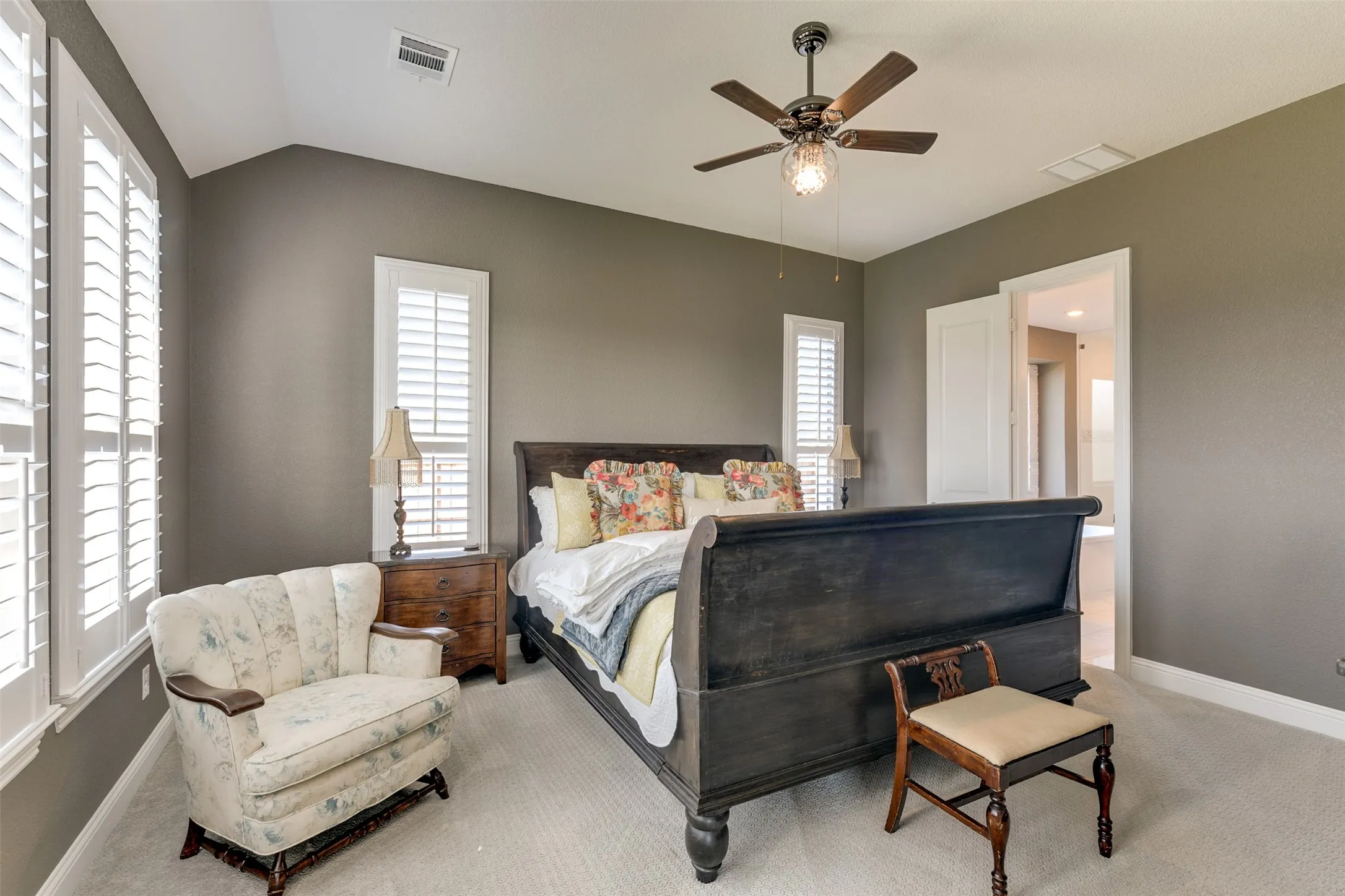 Carpeted bedroom featuring vaulted ceiling, multiple windows, and ceiling fan.  Windows open to the rear view enjoyed through a majority of the home