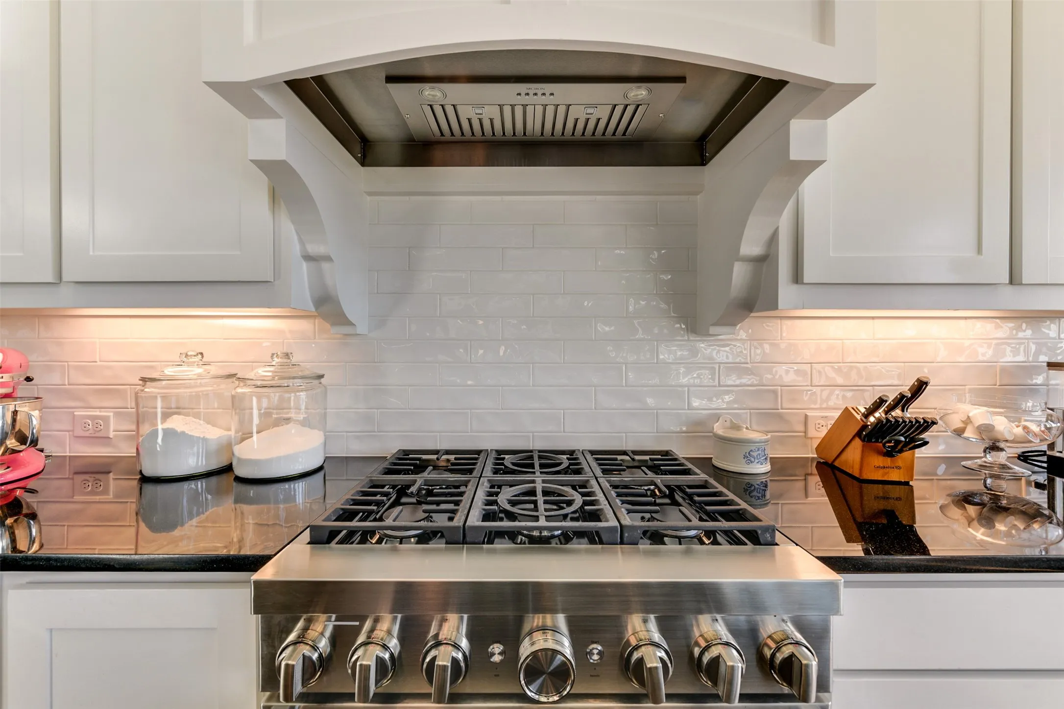 Kitchen featuring white cabinets, decorative backsplash, and six-burner range