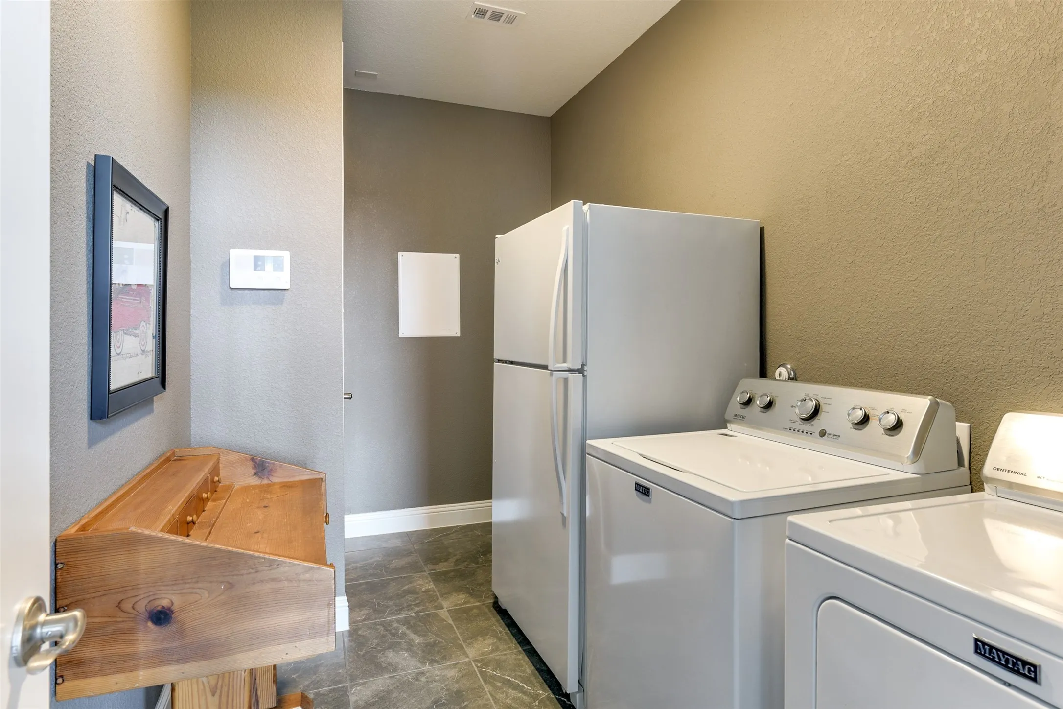 Laundry with dark tile patterned floors and washing machine and dryer.  Room for a full freezer if wanted