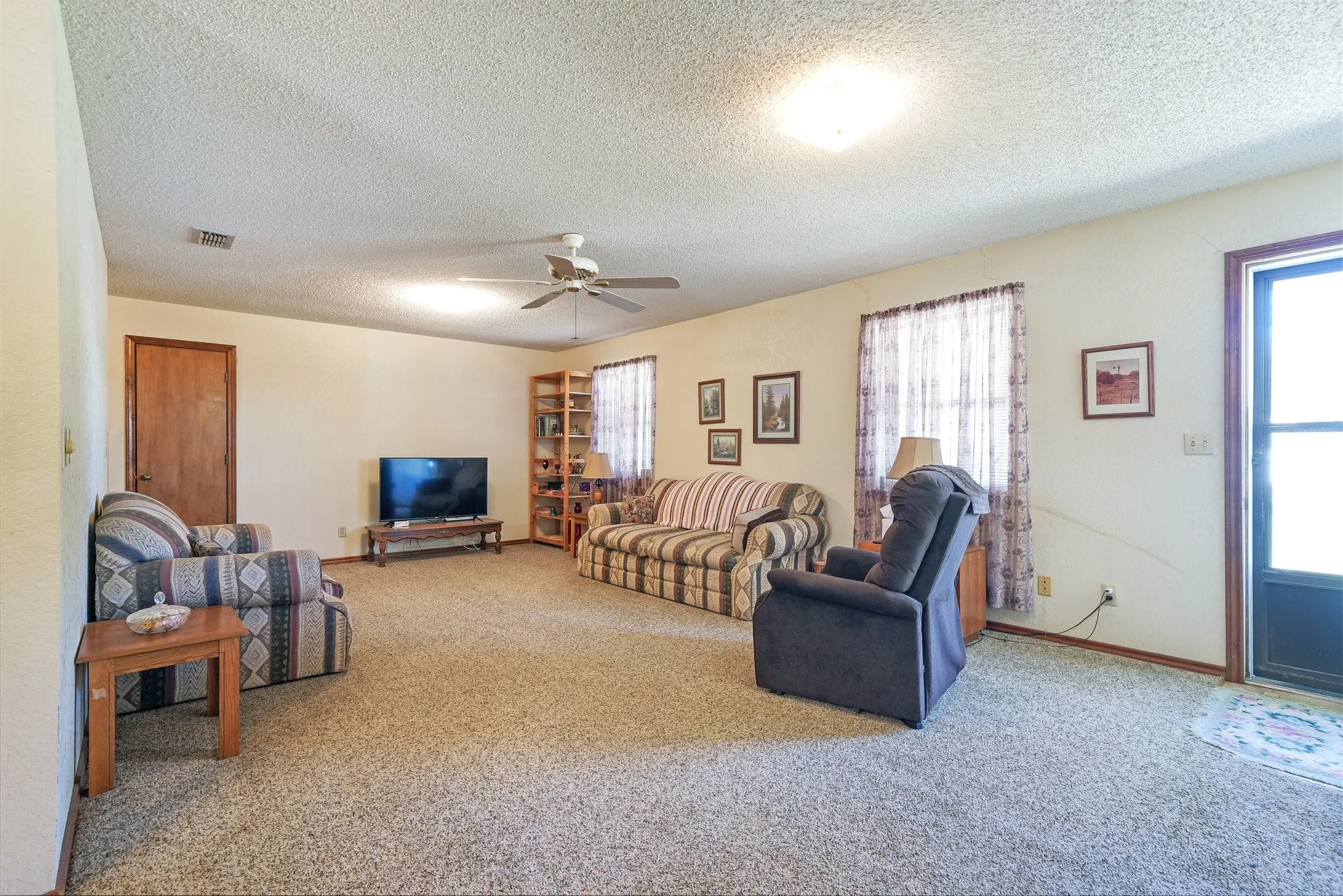 Carpeted living room with ceiling fan and a textured ceiling