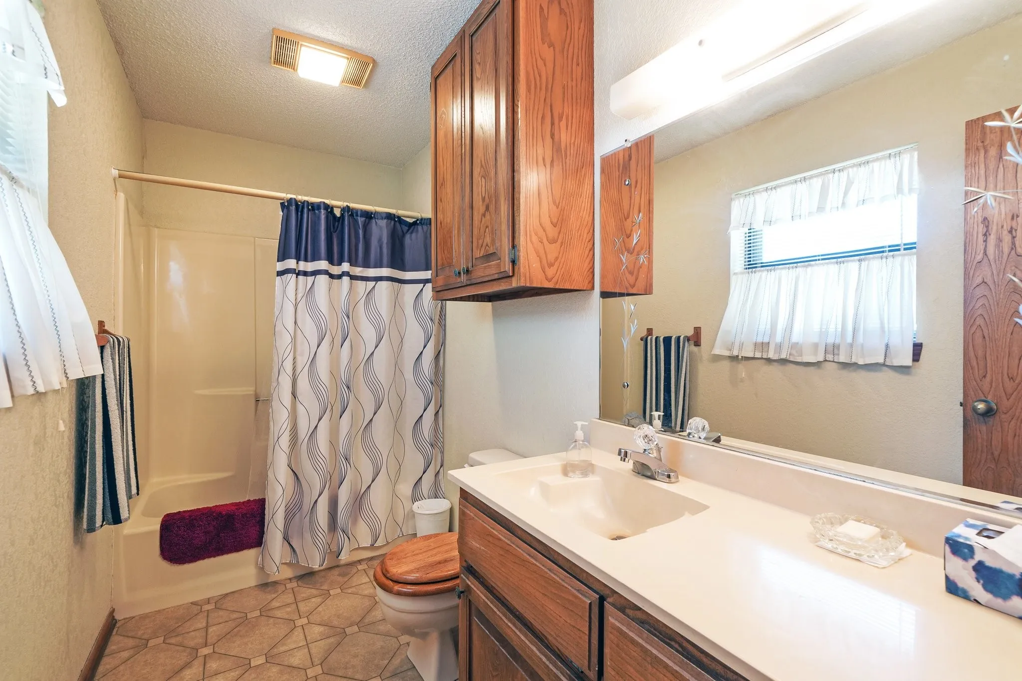 Full bathroom with vanity, a textured ceiling, shower / bath combo with shower curtain, tile patterned floors, and toilet