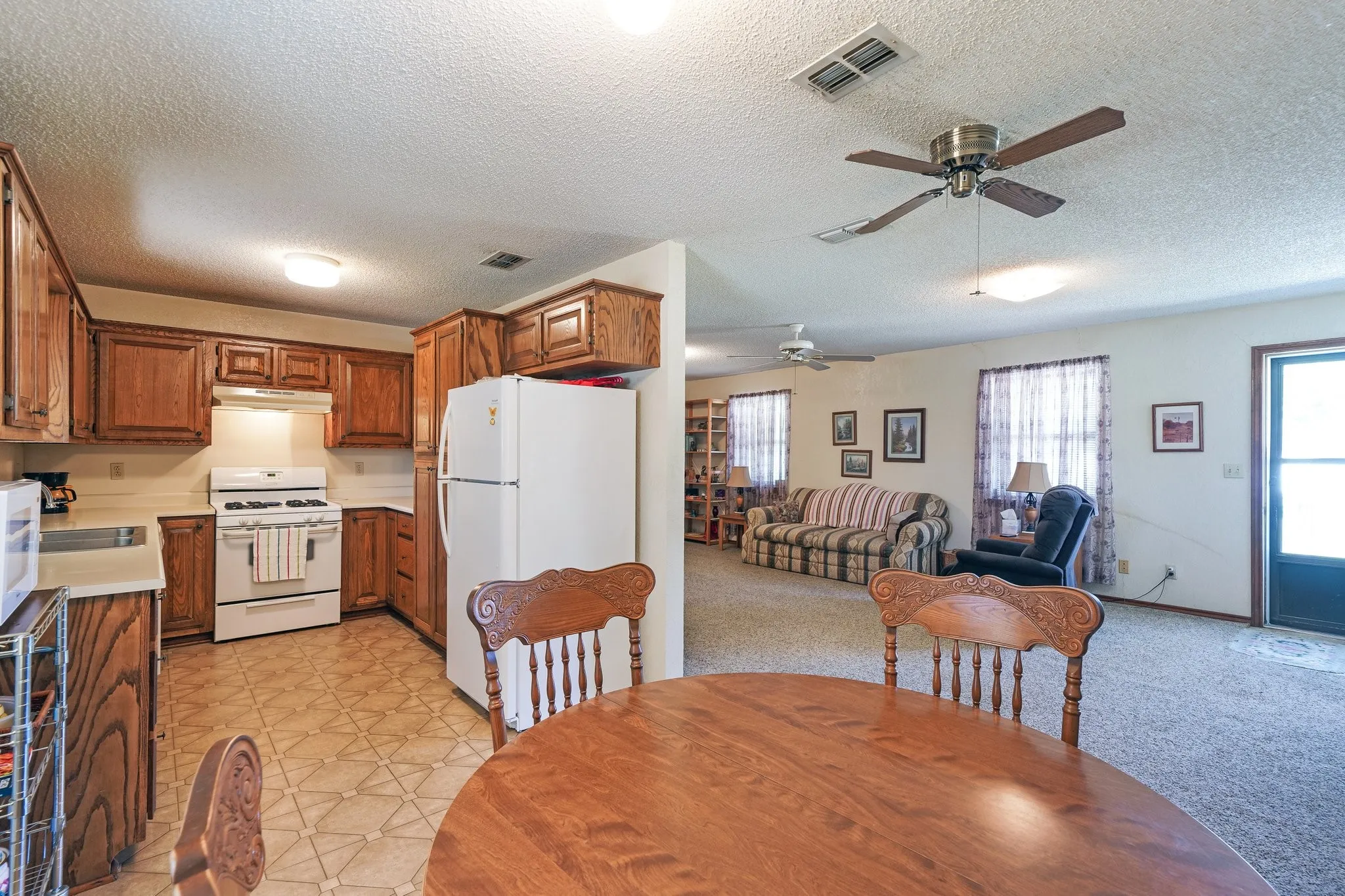 Kitchen with ceiling fan, light colored carpet, a textured ceiling, and white appliances