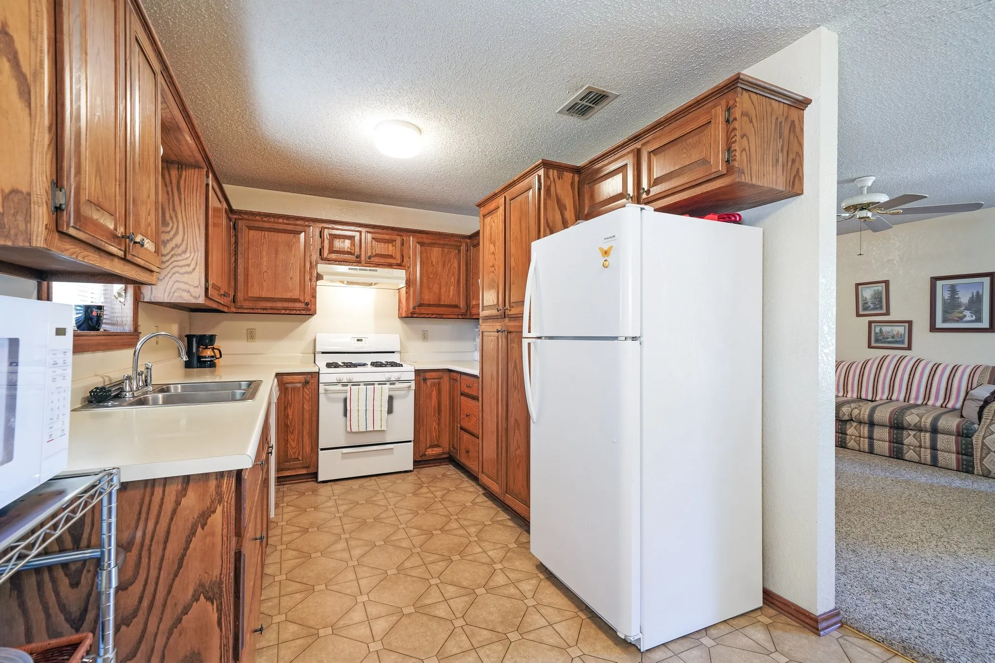 Kitchen featuring a textured ceiling, sink, light colored carpet, white appliances, and ceiling fan