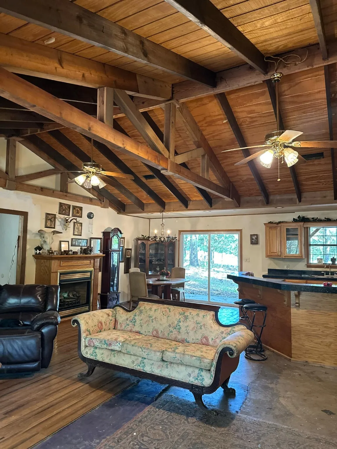 Living room featuring ceiling fan with notable chandelier, wooden ceiling, concrete flooring, and lofted ceiling with beams