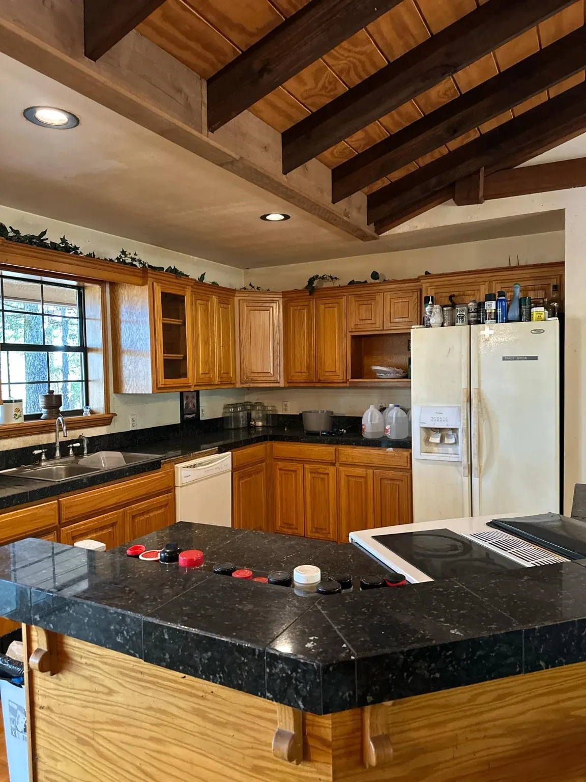 Kitchen featuring vaulted ceiling with beams, sink, white appliances, a kitchen island, and a kitchen breakfast bar